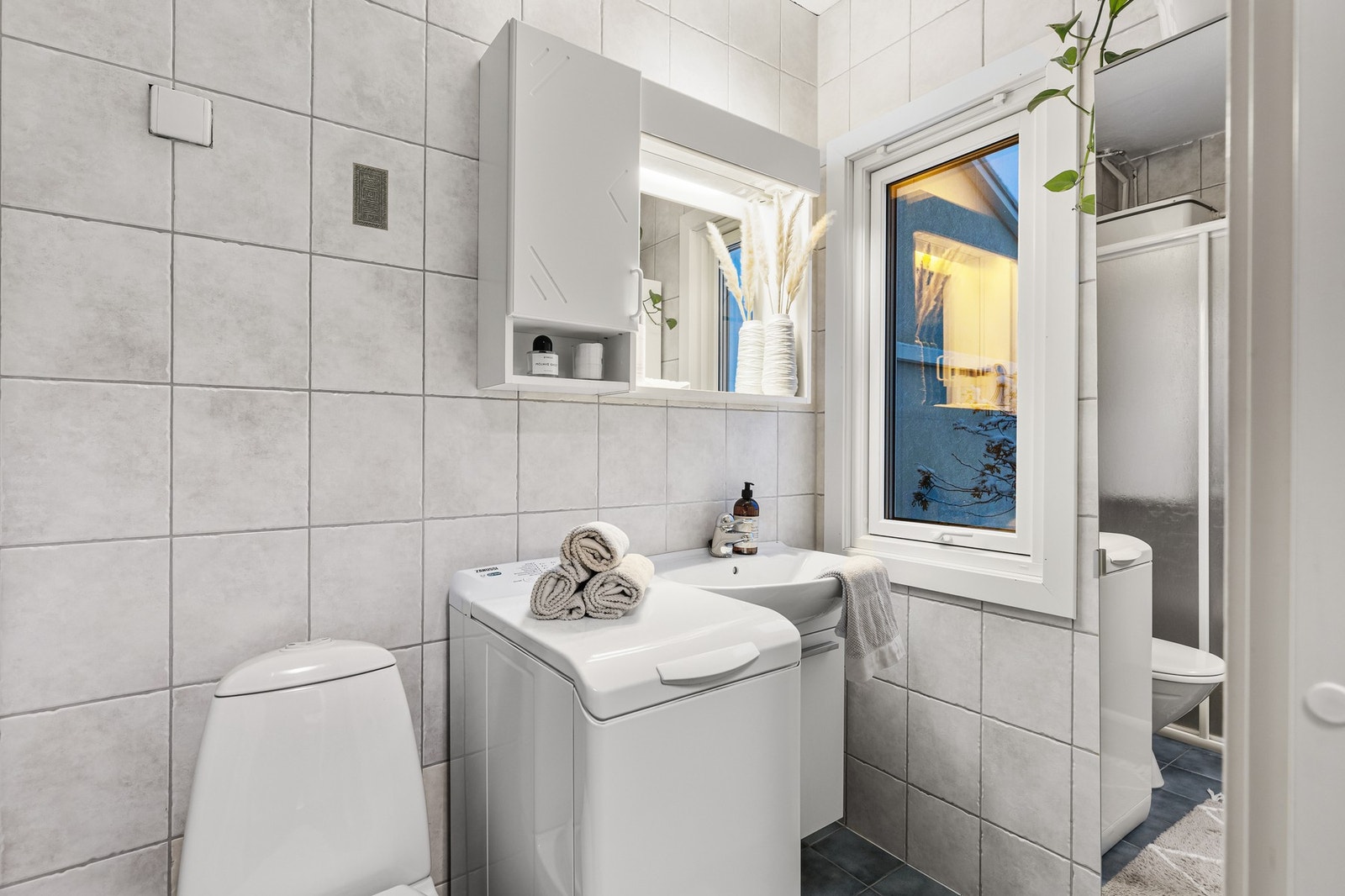 Flislagt bad på 3 kvm utstyrt med WC, servant over skap, speilskap og opplegg for vaskemaskin. I tillegg er det dusjsone og et høyskap. Galleribilde