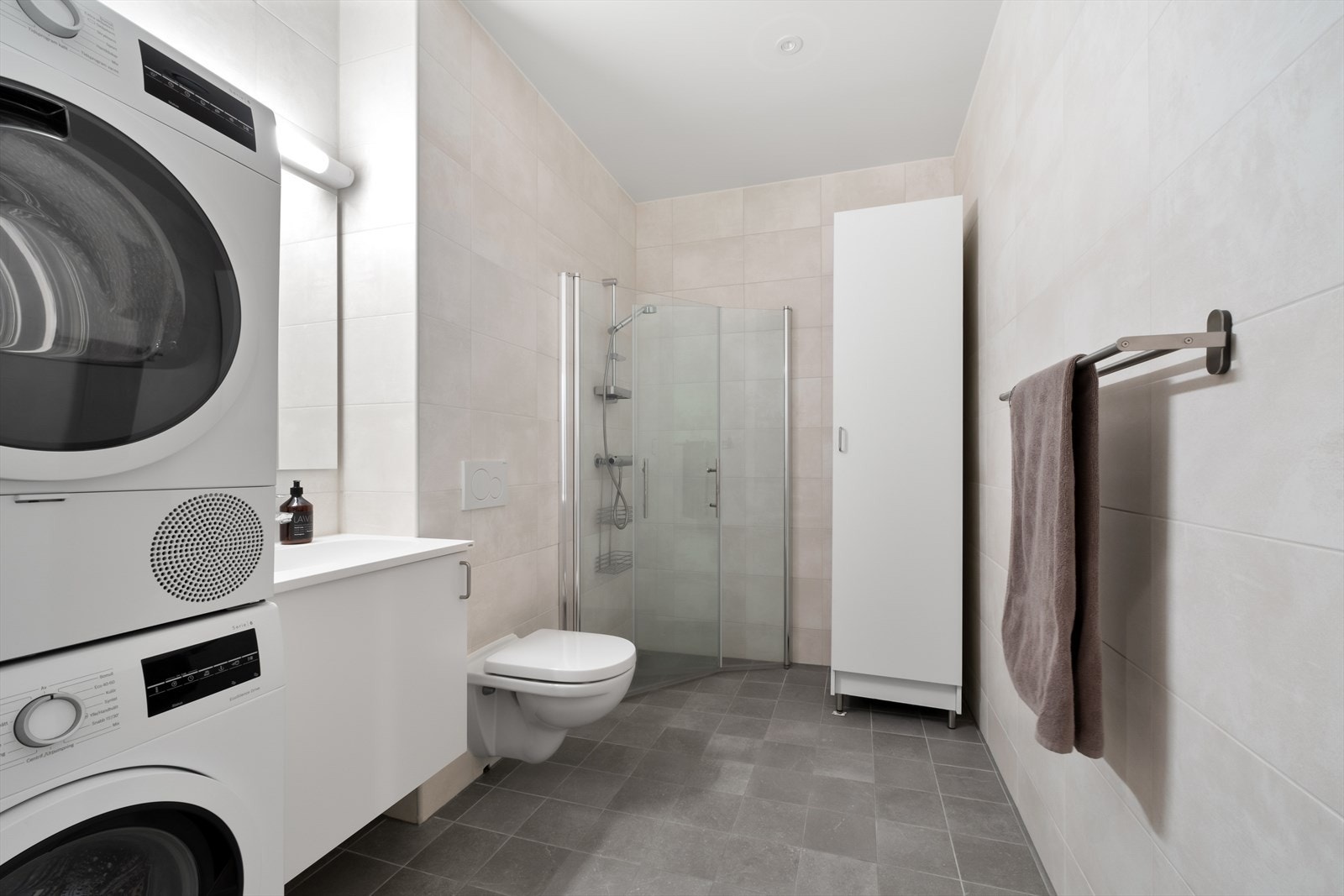 Moderne, flislagt bad med gulvvarme. Badet er utstyrt med dusj bak svingbare dører, toalett og servant. Galleribilde