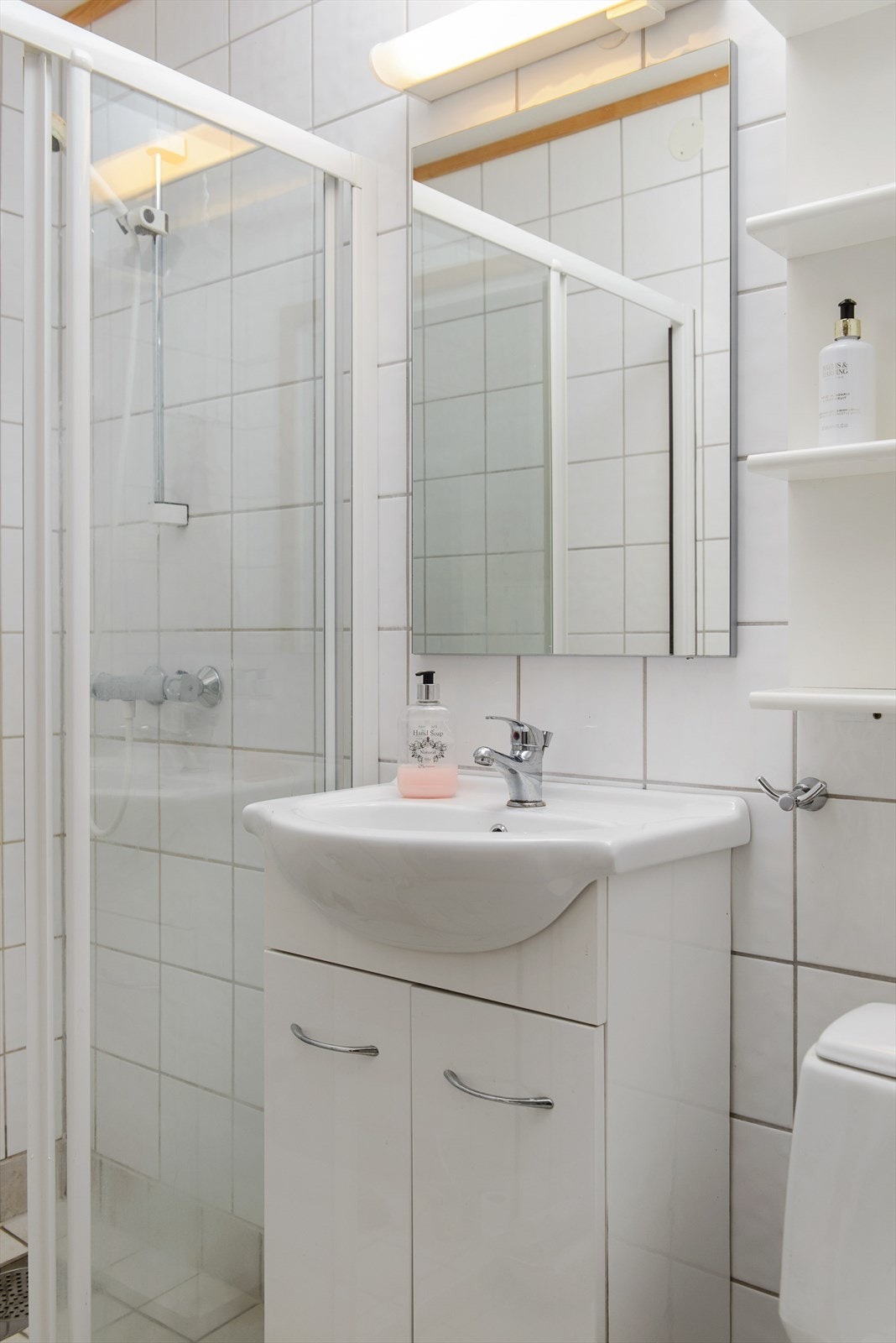 Lyst baderom med fliser på vegger og gulv. Videre er badet utstyrt med baderomsinnredning, servant, speil, toalett og dusj. Galleribilde