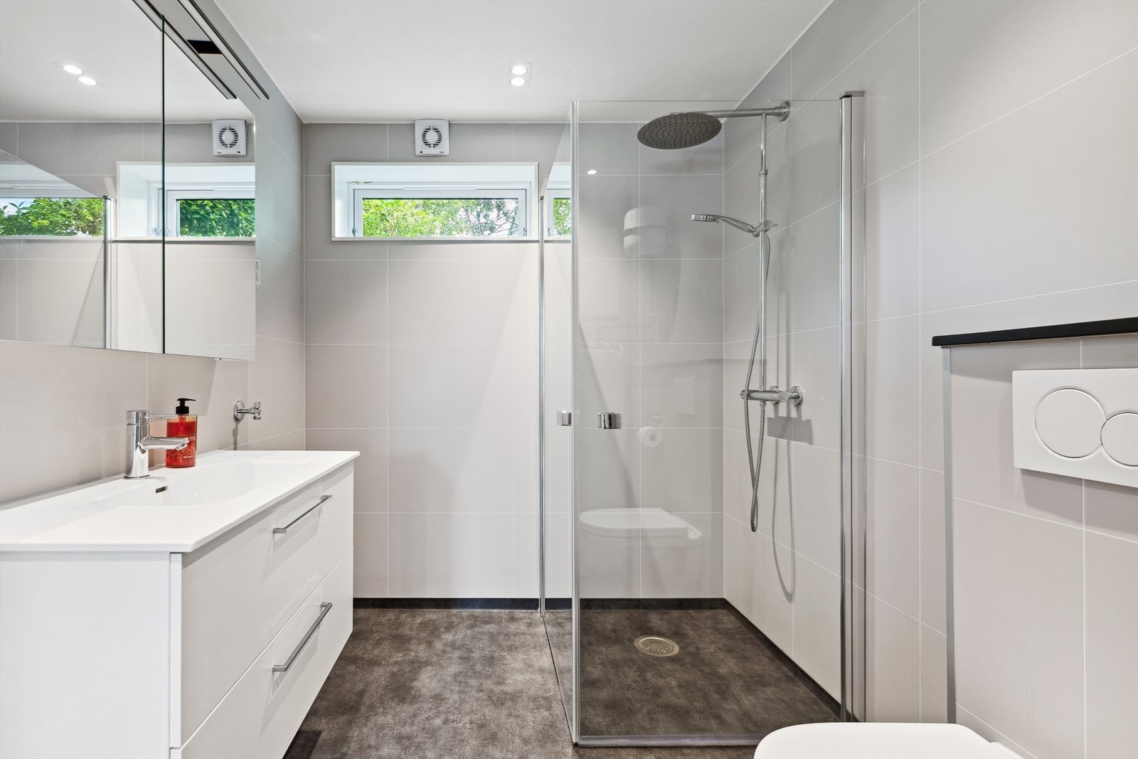 Baderom i utleiedelen med baderomsinnredning med servant, dusjhjørne, veggmontert toalett og opplegg for vaskemaskin Galleribilde