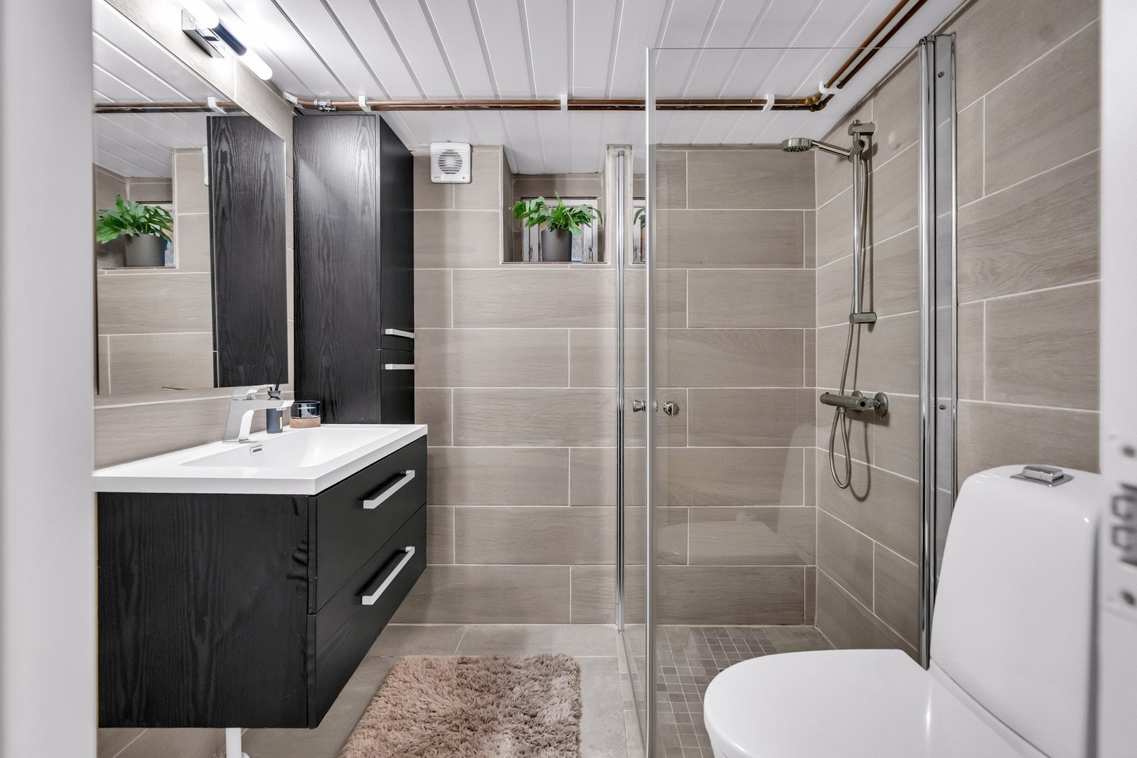 Moderne flisvvalg, mørk innredning og innfeldbare glassdører i dusjhjørne. Galleribilde