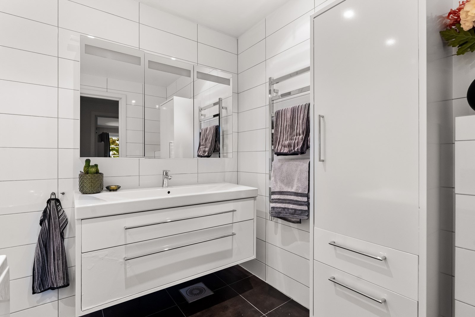 Videre er det montert veggmontert toalett, håndkletørker og høyskap, badekar med svingdør, håndholdt dusj og termostatstyrt blandebatteri. Galleribilde