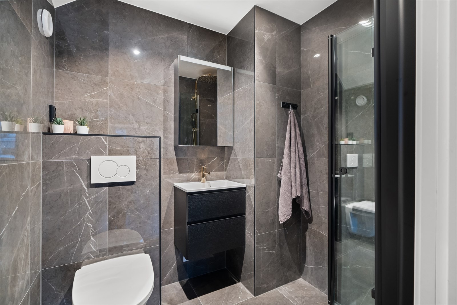 Badet er innredet med servantskap med heldekkende servant, samt speilskap på veggen. Videre er det tilkoblet veggmontert toalett, dusjhjørne med regnfallsdusj og termostatstyrt blandebatteri. Galleribilde