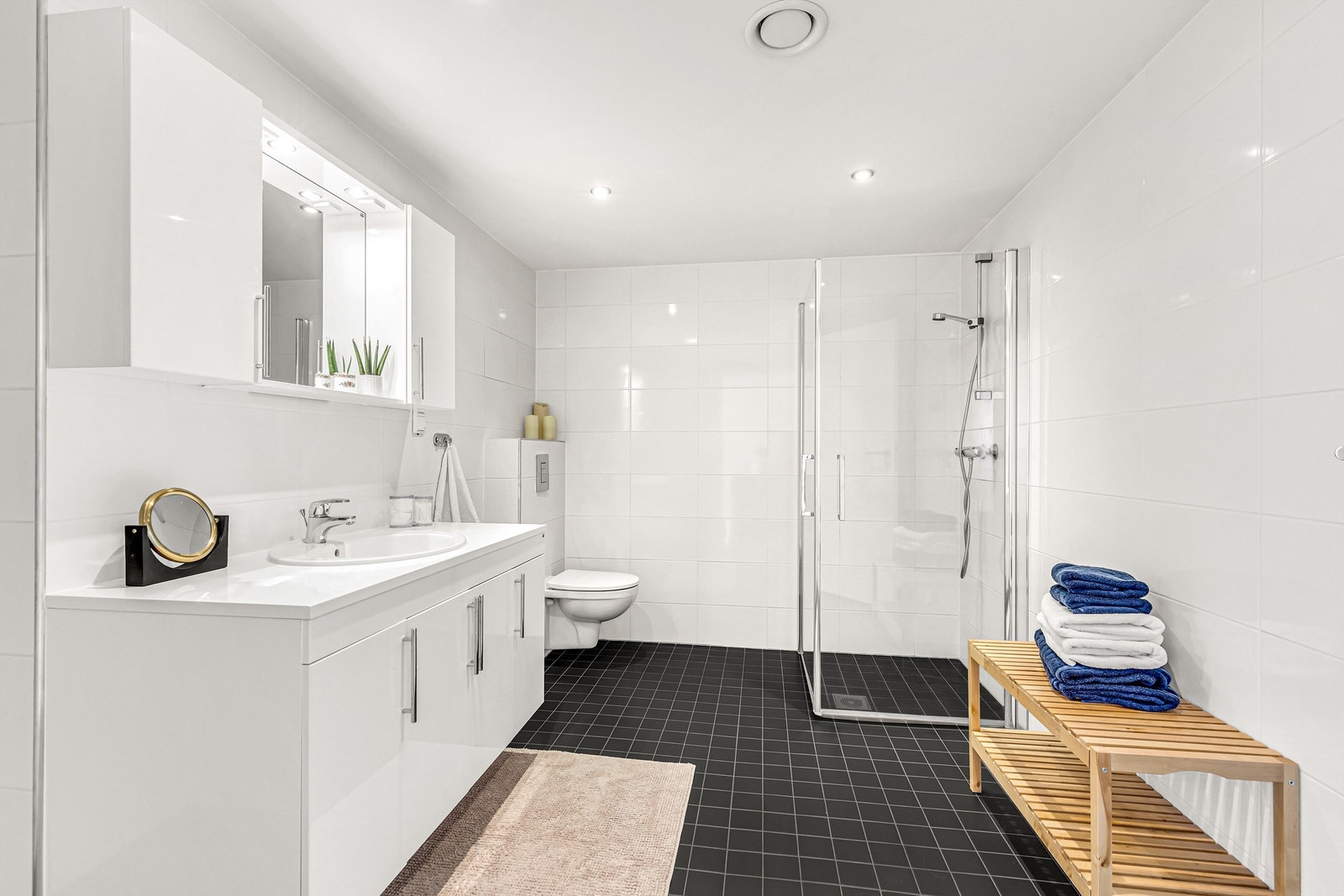 Delikat innredet bad med spotter i tak, dusjhjørne og vegghengt WC, samt romslig baderomsmøbel med belysning og speil Galleribilde