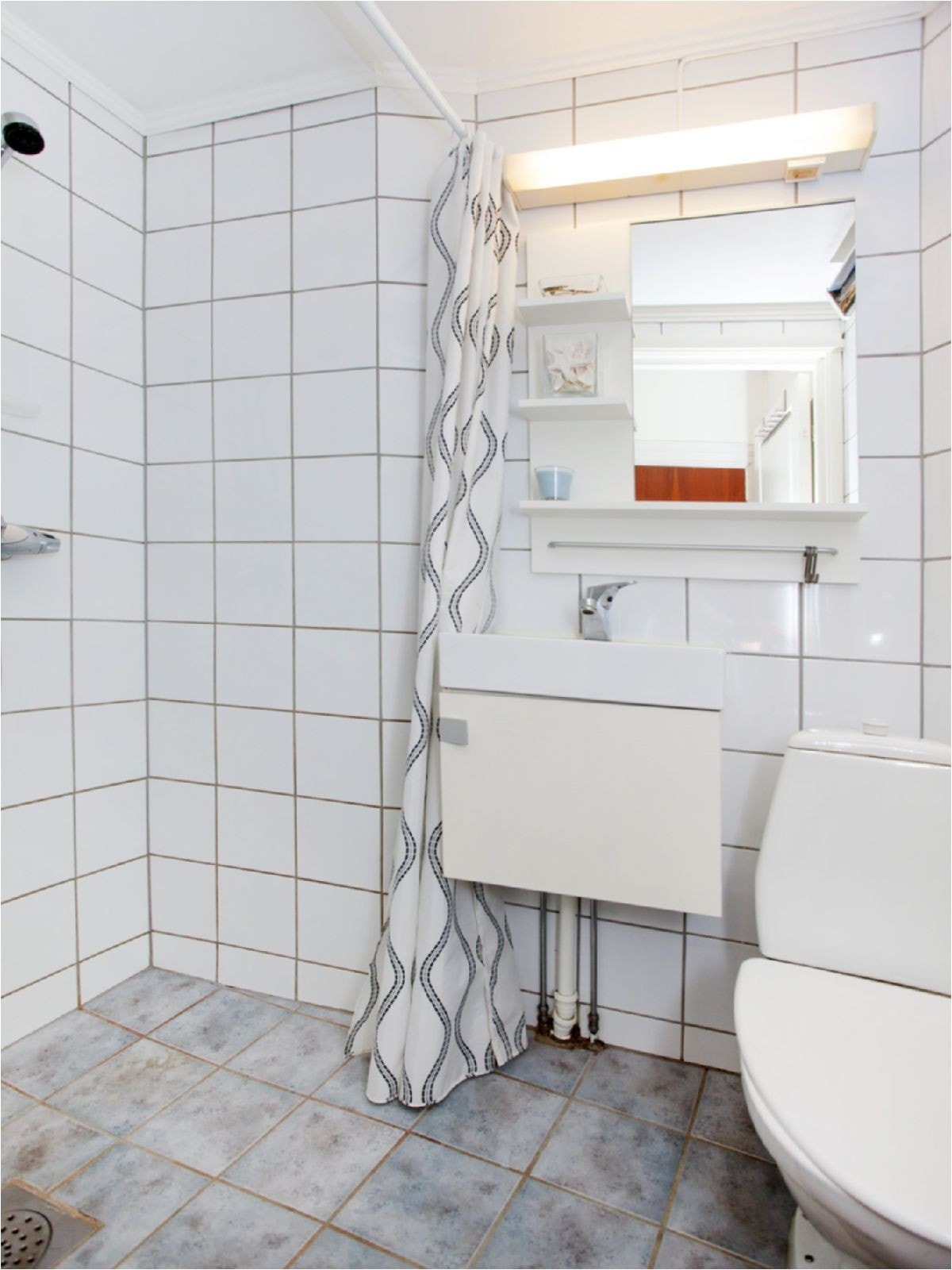 Pent flislagt bad innredet med dusjhjørne, wc og servant med unver- og overskap Galleribilde