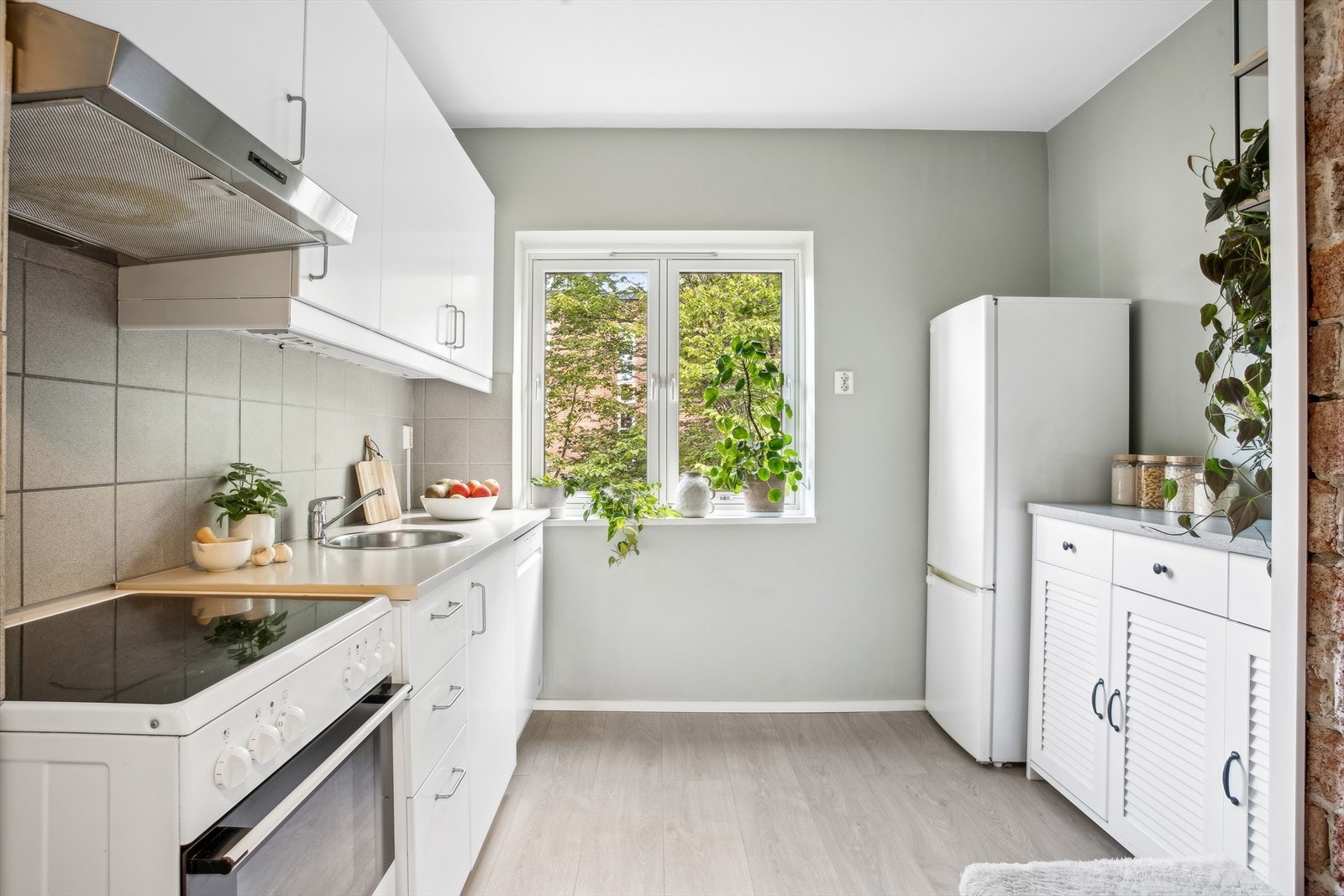 Kjøkkeninnredning med glatte fronter. Laminat benkeplate med nedfelt kum i rustfritt stål. Lys under overskap. Fliser på vegg over benk. Galleribilde