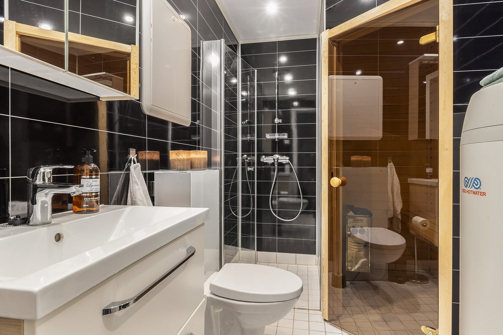 Stilrent baderom med våtromsplater på vegger og flislagt gulv. Dusjnisje, vegghengt toalett, baderomsinnredning med heldekkende servant. Galleribilde