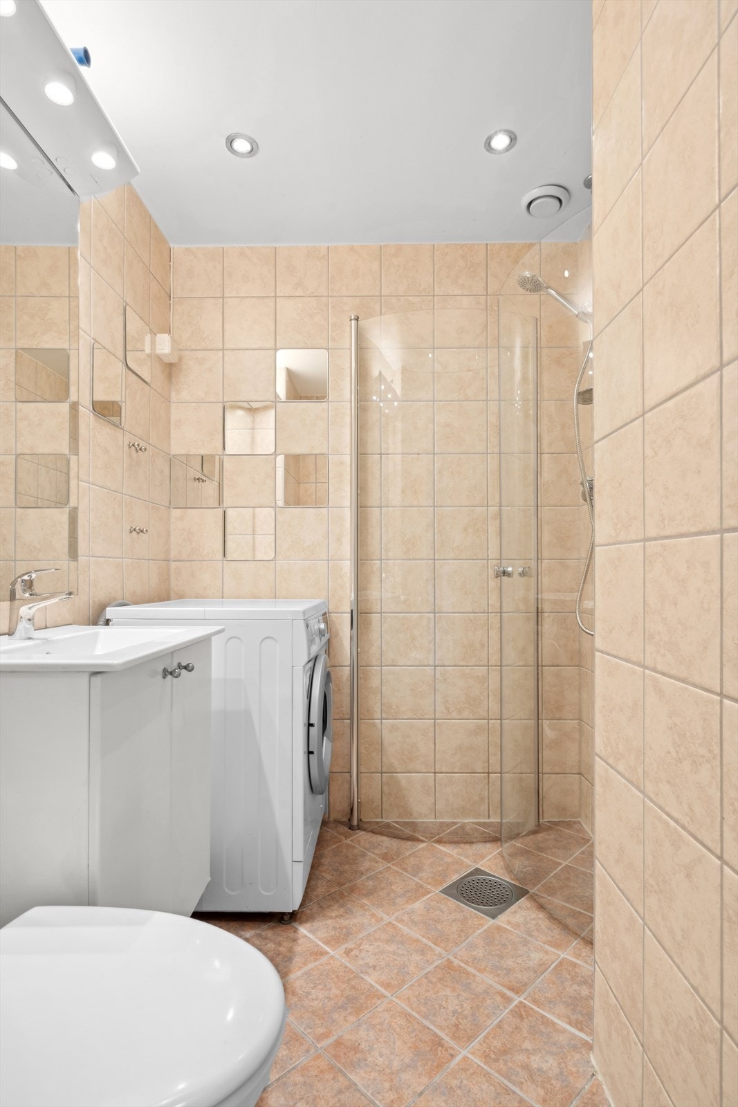 Pent flislagt baderom fra 2006 med dusjhjørne, vegghengt toalett, servant med underskap og opplegg til vaskemaskin. Galleribilde