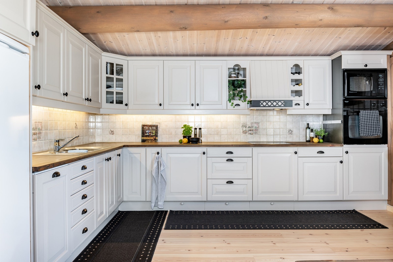 Et meget generøst kjøkken med heltre benkeplate, fliser mellom over- og underskap og delvis åpen og integrert løsning for hvitevarer Galleribilde