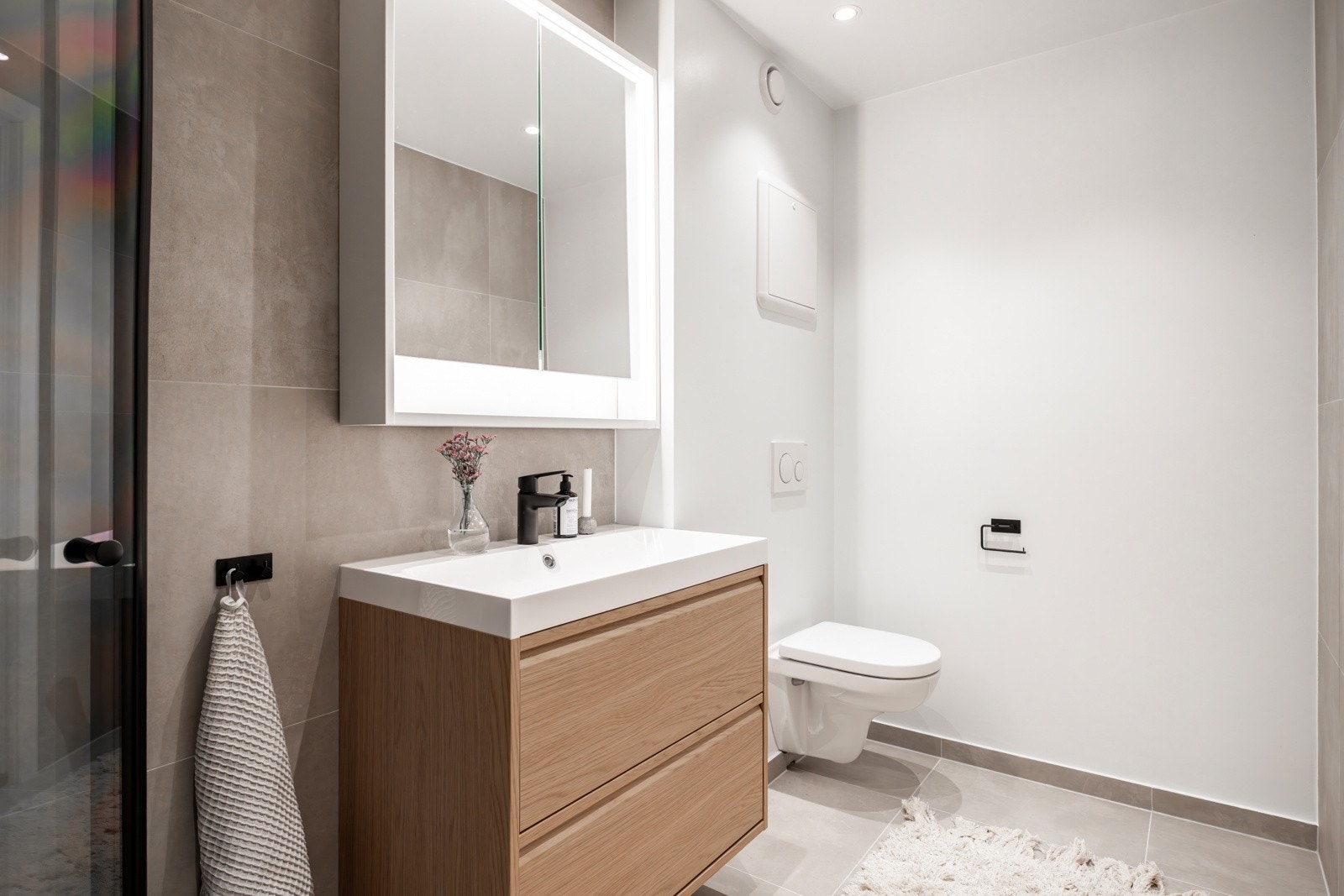 Store grå fliser i en lun og delikat tone kombineres med slette veggflater for en moderne og ren stil. Badet har opplegg for vaskemaskin og tørketrommel samt varmekabler for ekstra komfort. Galleribilde
