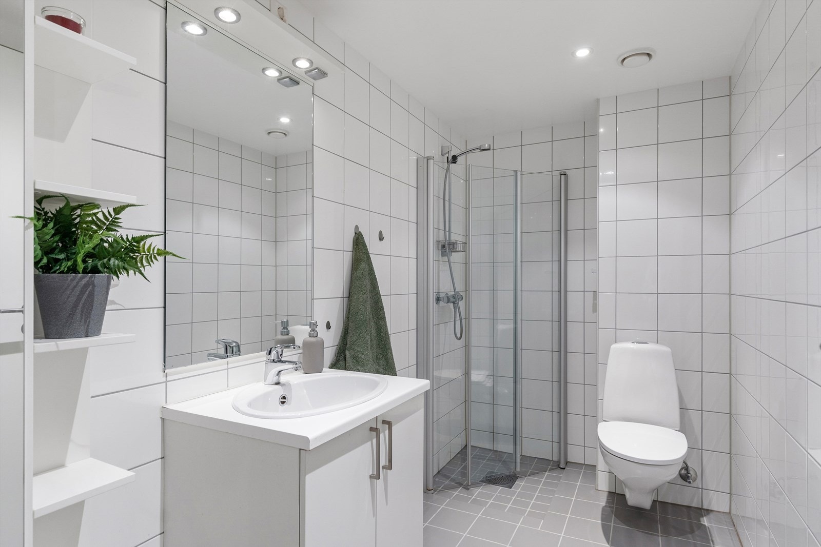 Et meget innbydende baderom med varmekabler i gulvet, servant, vegghengt toalett og dusj med svingbare dører i herdet glass. Høyskap med speilfront gir praktisk oppbevaring, mens servantskapet har stilrene, hvite fronter. Galleribilde