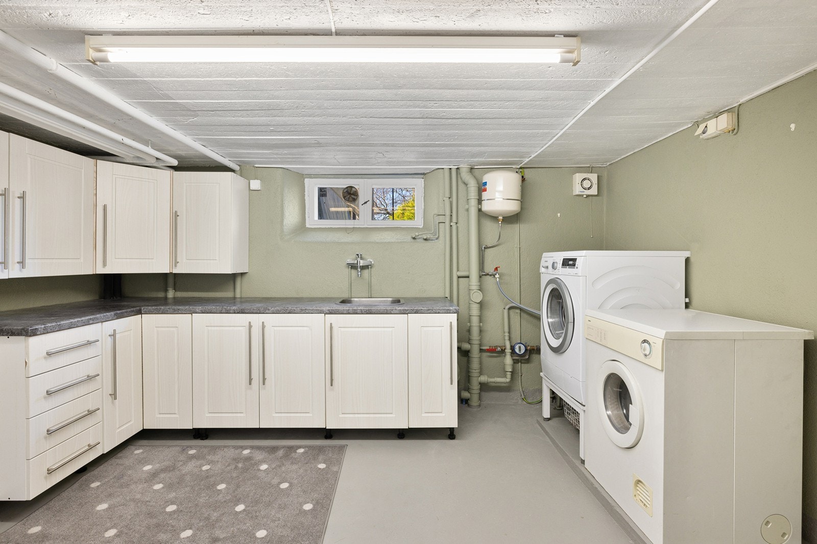 Et stort og praktisk vaskerom ligger i underetasjen med malt betong på gulv og malte pussede vegger som ble oppgradert i 2023. Her er det ekstra arbeidsflater og god oppbevaringsplass i både underskap/overskap. Galleribilde