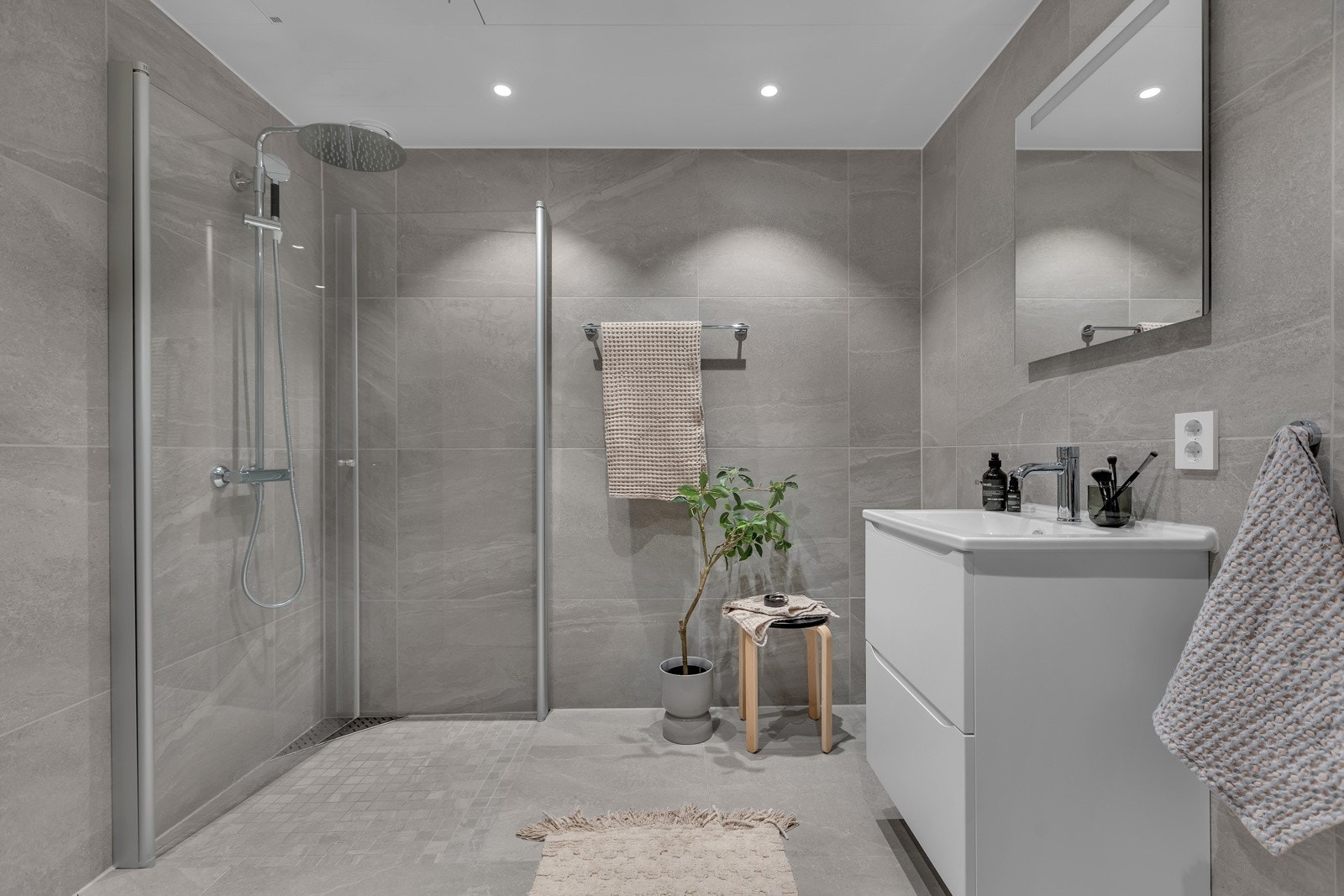 Pent bad med fliser på gulv og vegger, innfellbare glassdører i dusjsonen, praktisk innredning med hedekkende servant og lagring i underskap Galleribilde