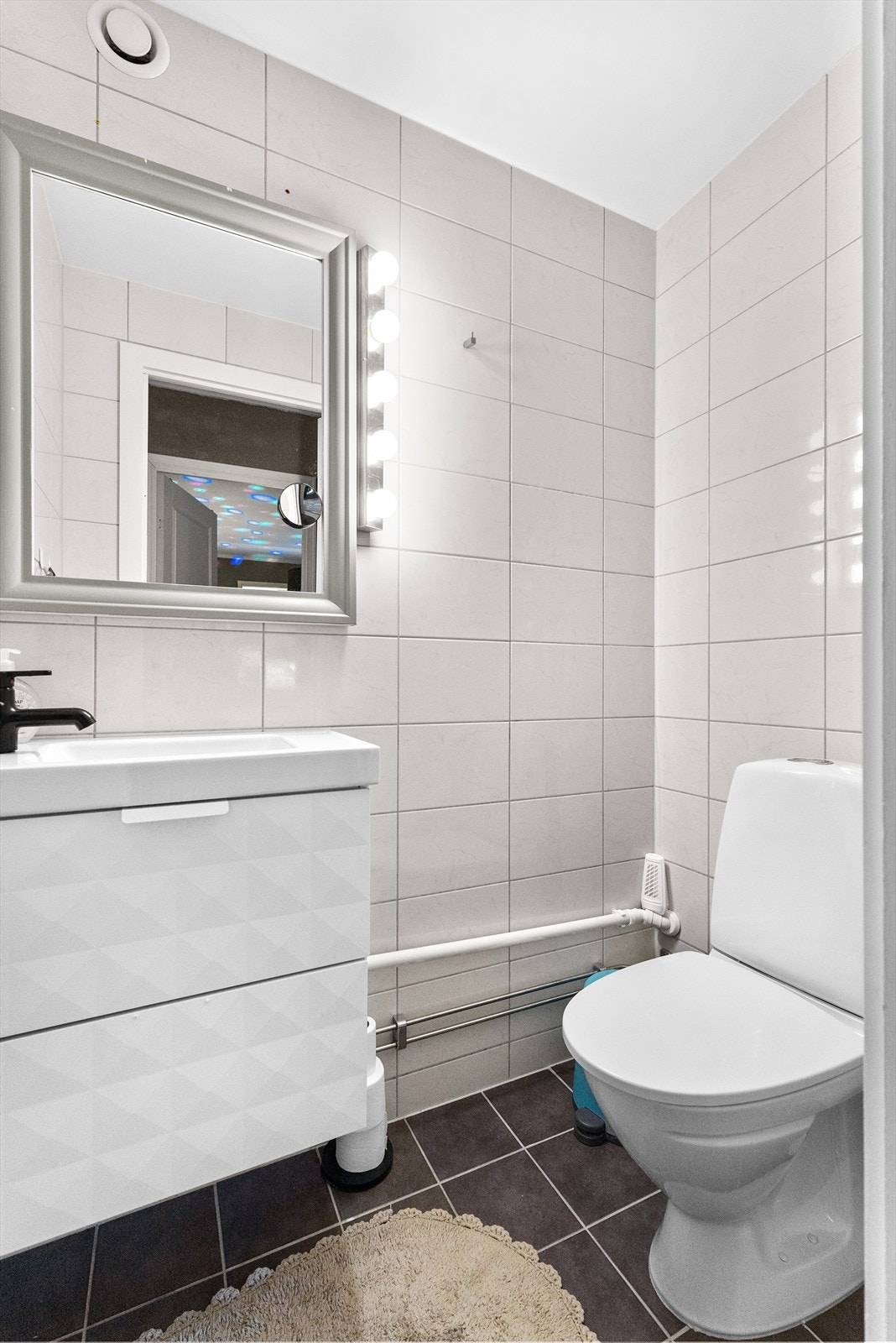 Toalettrommet er helfliset og har en pen, hvit servantinnredning, speil og toalett. Galleribilde