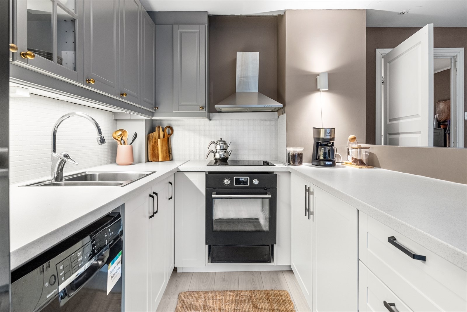 Kjøkkenet har benkeskap med hvite rammefronter, veggskap med grå fronter, noen vitrinedører og benkeplate i laminat. Galleribilde