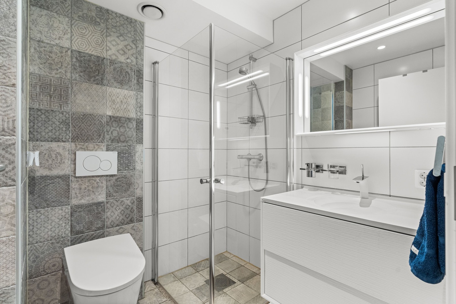 Baderomsinnredningen er bestående av vegghengt servantskap med profilerte fronter, nedsenket servant med ett-greps armatur, vegghengt speilskap med integrert lys, dusjhjørne med innfellbare glassdører og dusjarmatur tilkoblet hånddusj og vegghengt Geberit Galleribilde