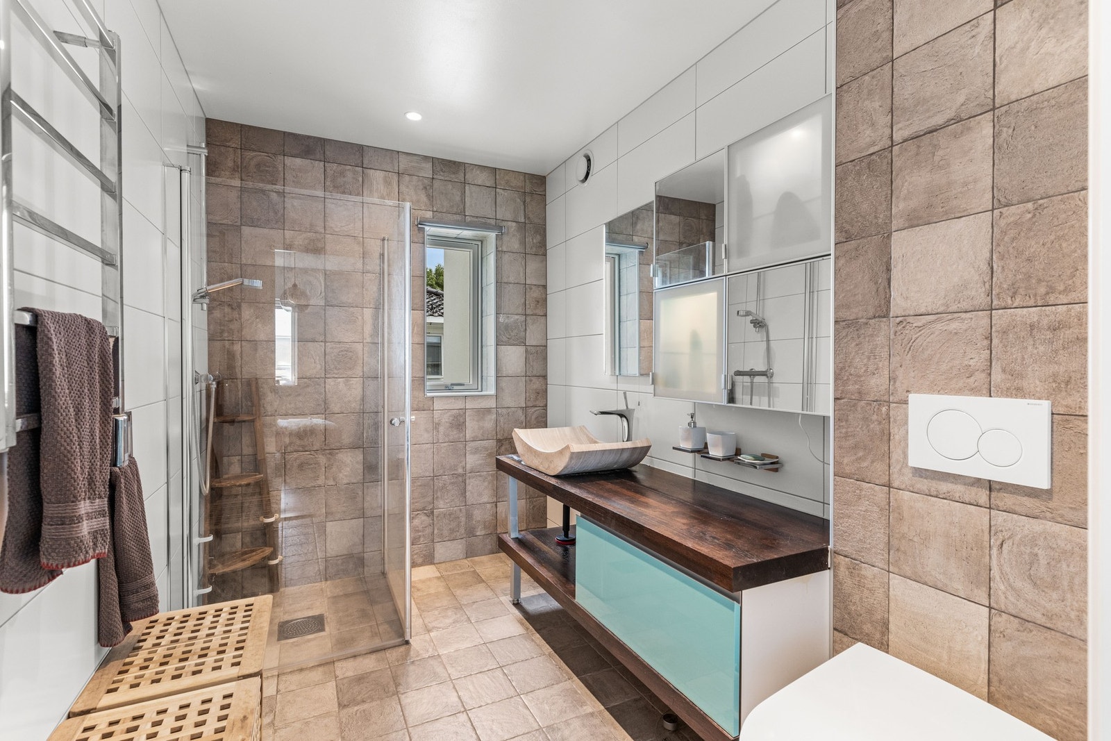 Badet er fra 2017 og har flislagt gulv med gulvvarme og flislagte vegger. Gulvstående innredning med glatte fronter og ovenpåliggende servant med ett-greps armatur, vegghengt speil med integrert lys, vegghengt servantskap og dusjhjørne med innfellbare gla Galleribilde