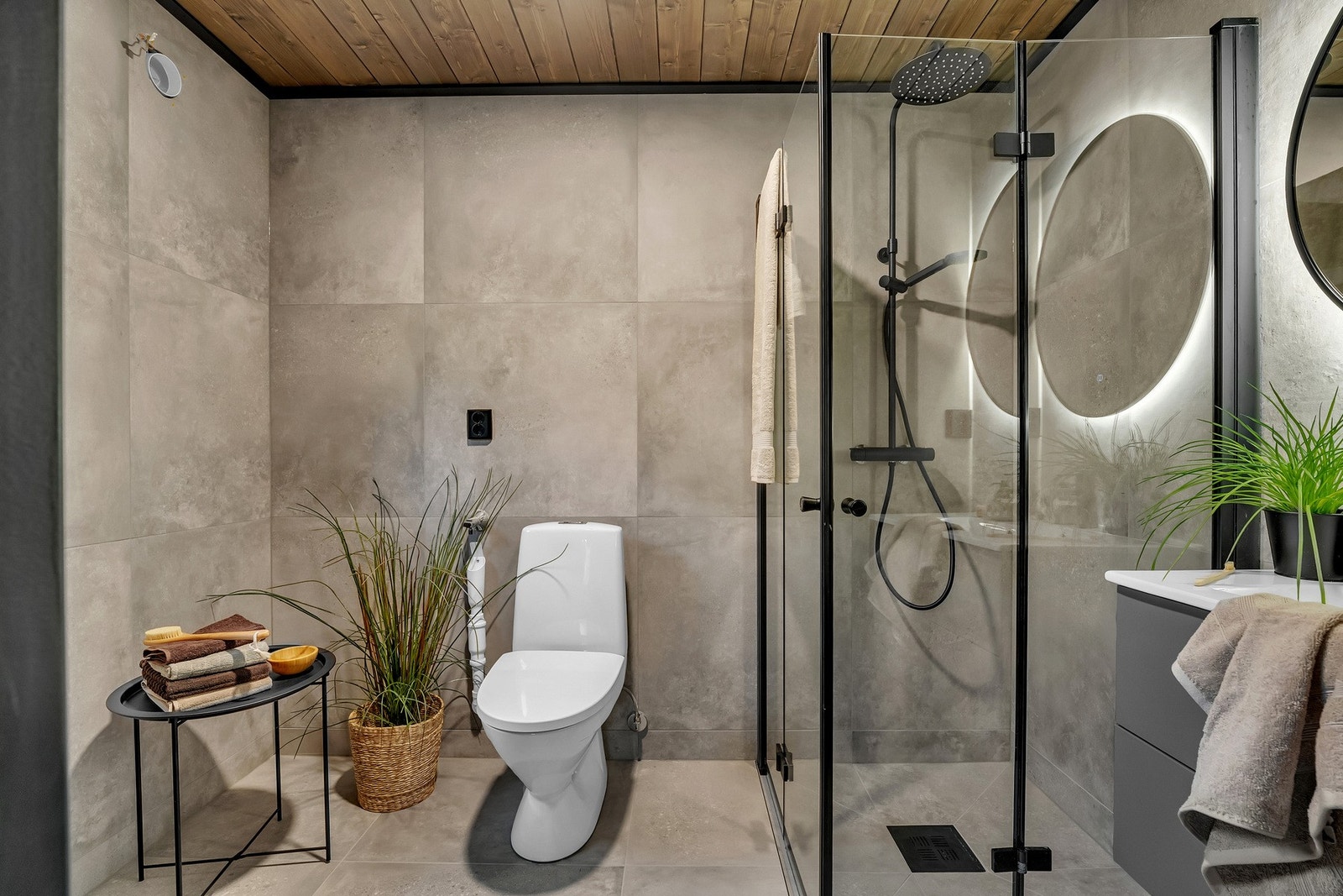 Dette rommet er tilknyttet et av to baderom med gulv og vegger i store fliser, kombinert med trehimling for et naturlig preg. Begge badene er utstyrt med dusjvegger, gulvstående toalett og vegghengt servant. Galleribilde