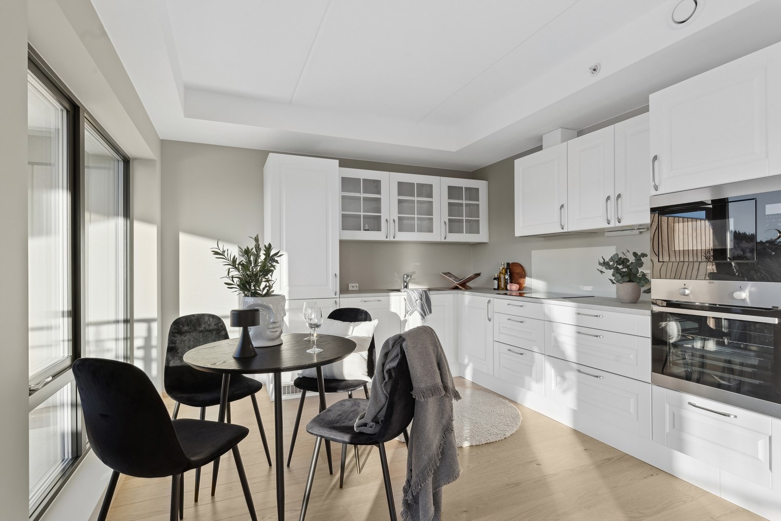 Kjøkkeninnredningen består av lyse folierte fronter i lys farge. Glassfelt i overskap ved vask. Laminerte benkeplater med nedfelt oppvaskkum i kompositt. Lys under overskap ved koketopp. Galleribilde