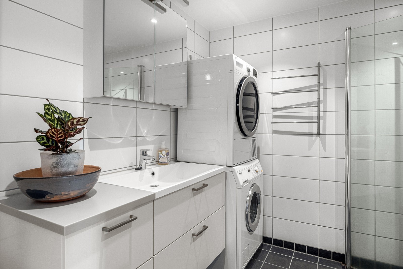 Badet er pent innredet med servantskap med oppbevaringsskuffer, speilskap og dusjløsning med innfellbare glassdører. Det er avsatt plass til vaskemaskin og tørketrommel i søyleløsning. Galleribilde