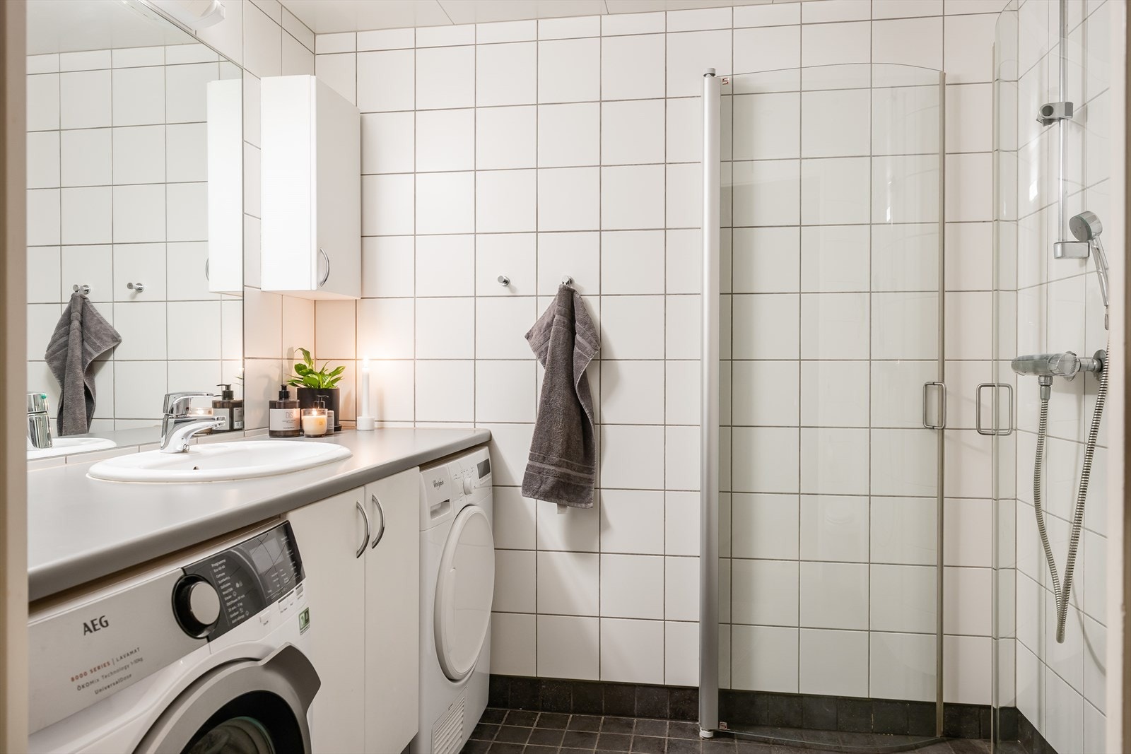 Badet har dusjhjørne med innfelbare dusjdører, vegghengt toalett og servantinnredning med nisje til vaskemaskin og tørketrommel. Galleribilde