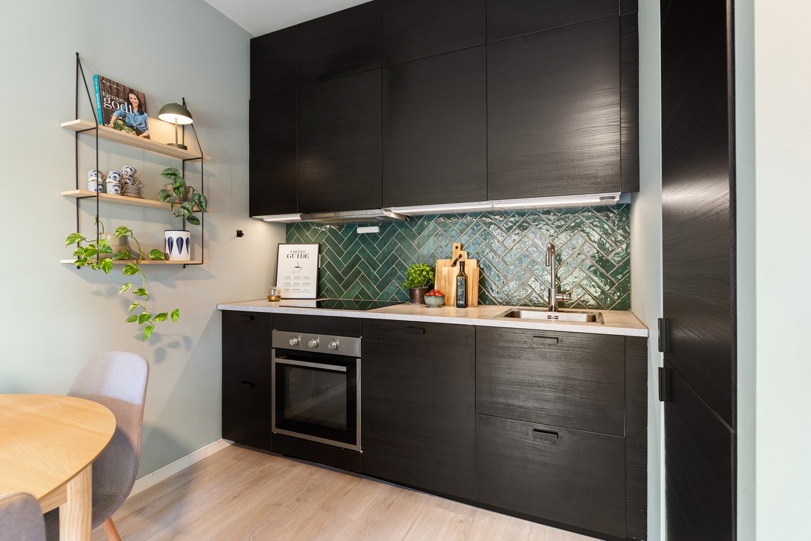 Pent kjøkken med mørke, slette fronter som gir et moderne uttrykk. Overskapene er utstyrt med benkebelysning som gir god arbeidsbelysning, og veggen er kledd med fliser for et stilrent preg Galleribilde