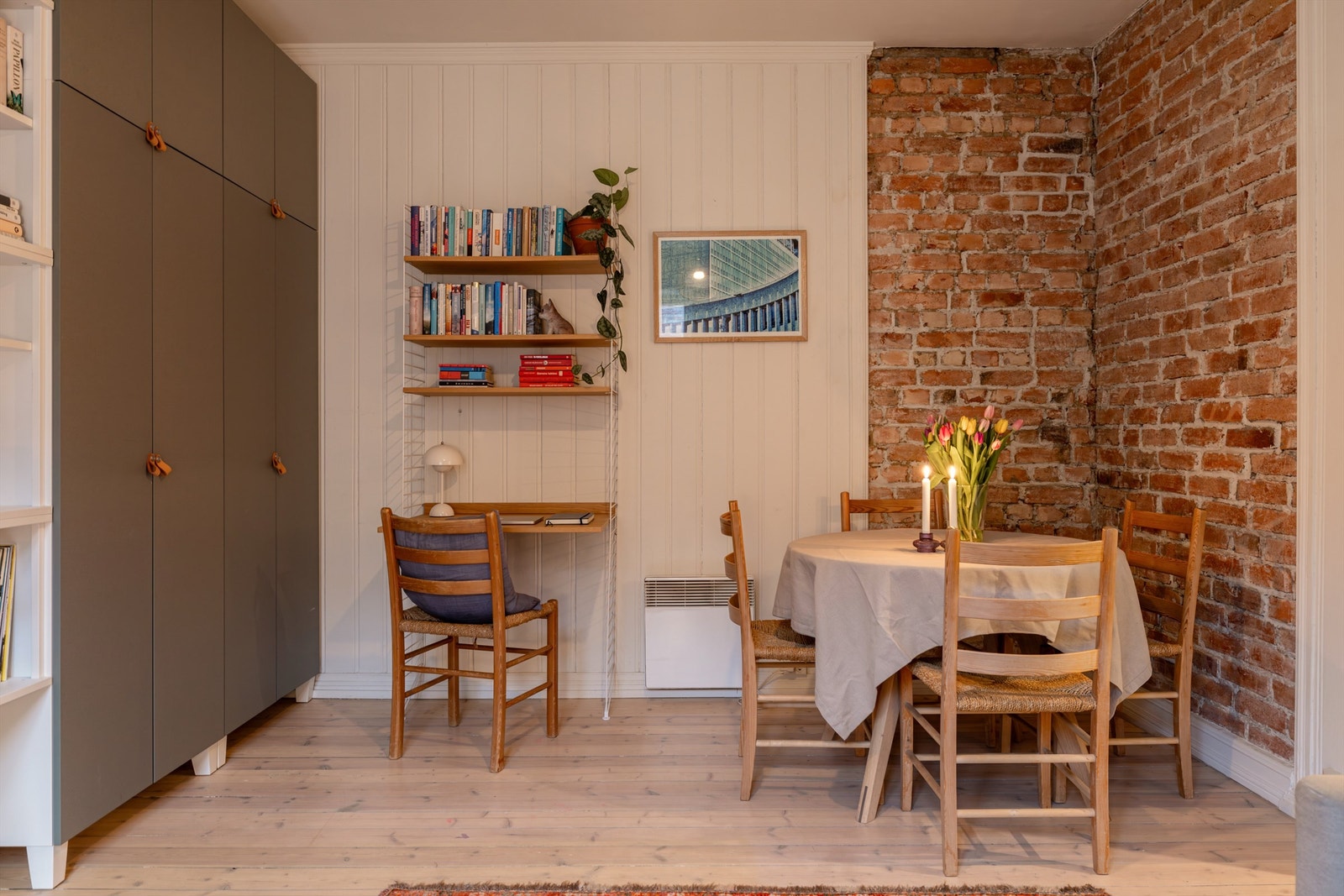 Pen stue med originale tregulv, hvitmalte panelvegger og en stilig kontrastvegg der teglsteinen er hentet frem. Galleribilde