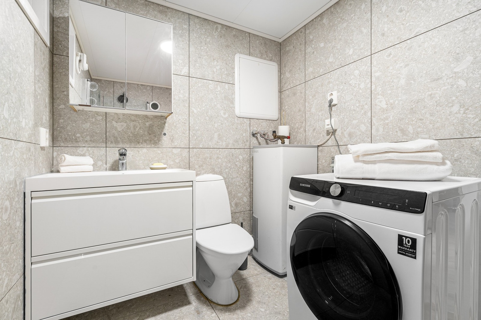 Badet er utstyrt med opplegg for vaskemaskin, varmtvannsbereder og dusjhjørne med innfellbare dører. Galleribilde