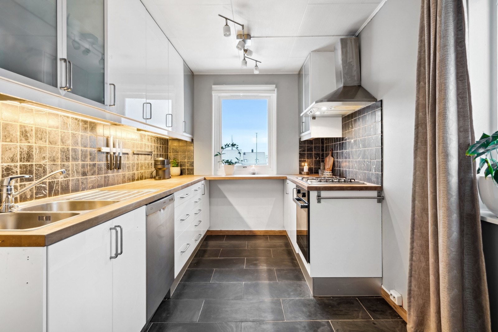 Kjøkkenet ligger delvis tilbaketrukket fra stuen, skjermet fra stuen for å kunne fokusere på maten, men fortsatt åpent nok til sosialt samvær. Galleribilde