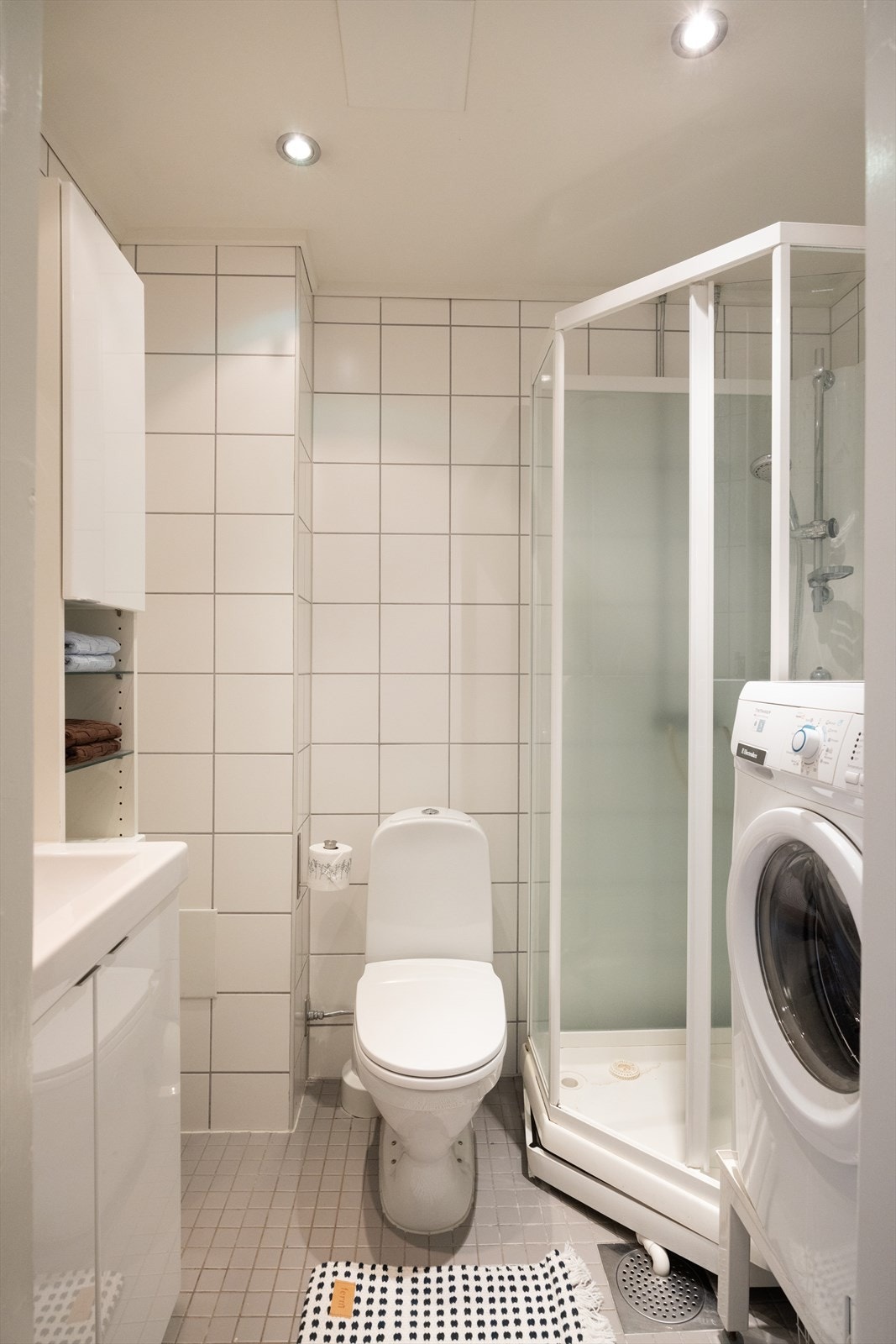 Badet inneholder servant med innredning, skap, toalett, dusjkabinett og opplegg til vaskemaskin. Galleribilde