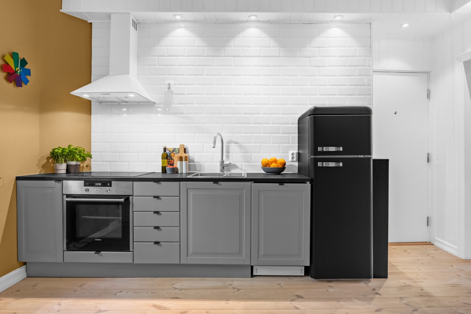 Innredningen er plassert langs én side og har grå, profilerte fronter med soft close og benkeplate i sort laminat med nedfelt vaskekum i stål. Galleribilde