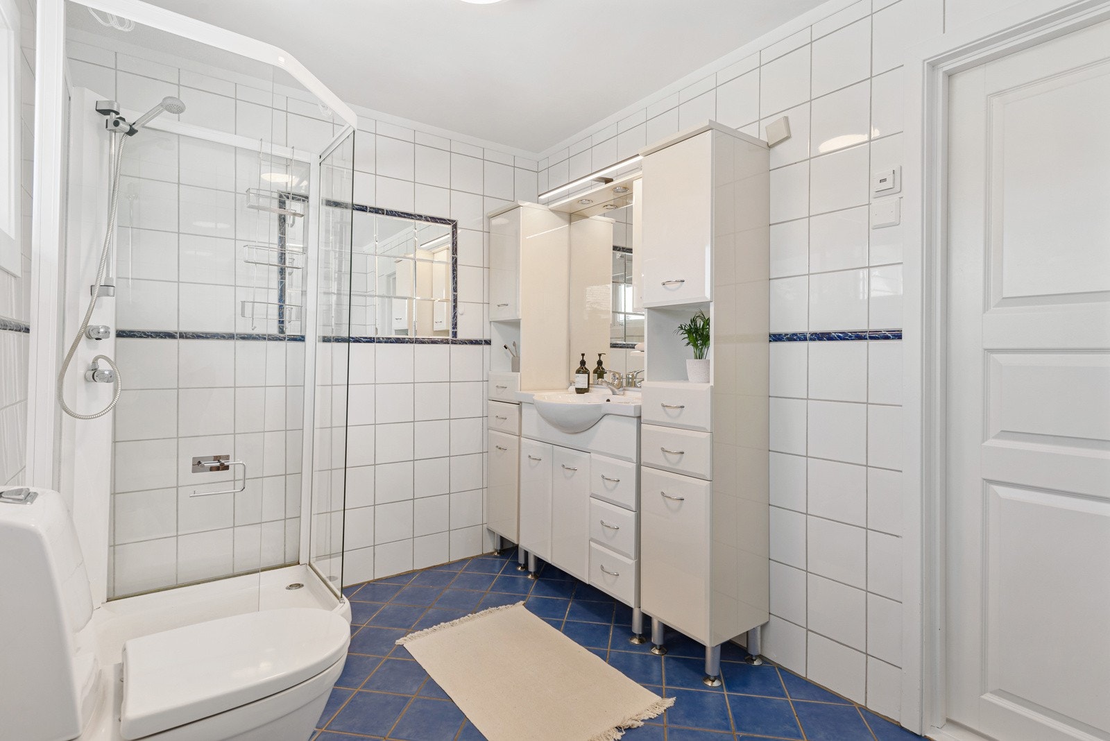 Badet har god størrelse, innredet med hvite veggfliser og mørkeblå fliser på gulvet. Galleribilde