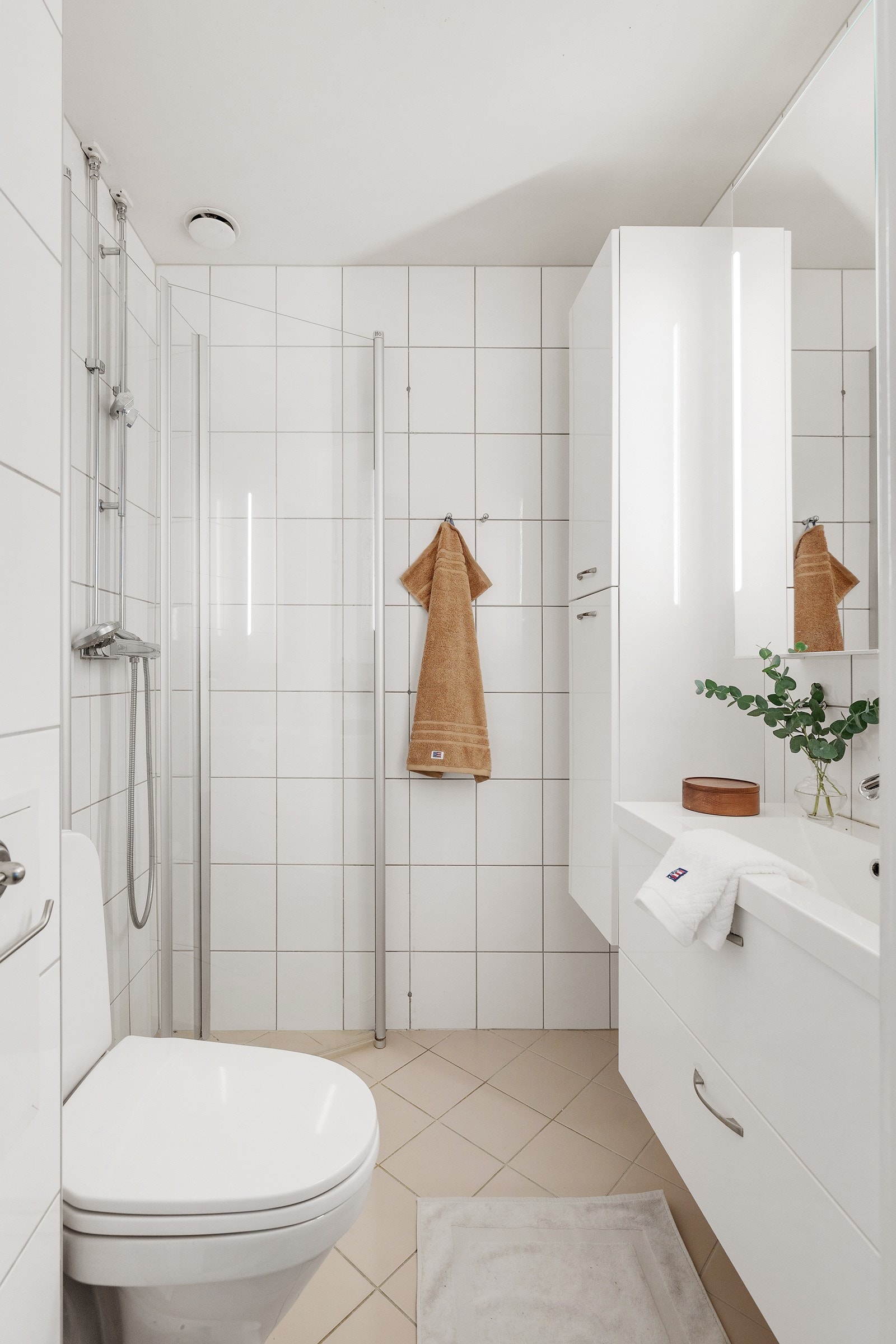 Badet er utstyrt med et gulvmontert toalett, servantinnredning, og dusjhjørne med dusjdører i glass Galleribilde