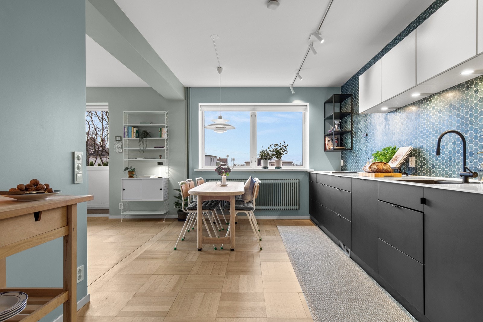 Den lyse Corian-benkeplaten med underlimt sort komposittvask og matchende ett-greps armatur i sort gir et eksklusivt preg. Kjøkkenet er utstyrt med integrerte hvitevarer av høy kvalitet fra Miele og Siemens Galleribilde