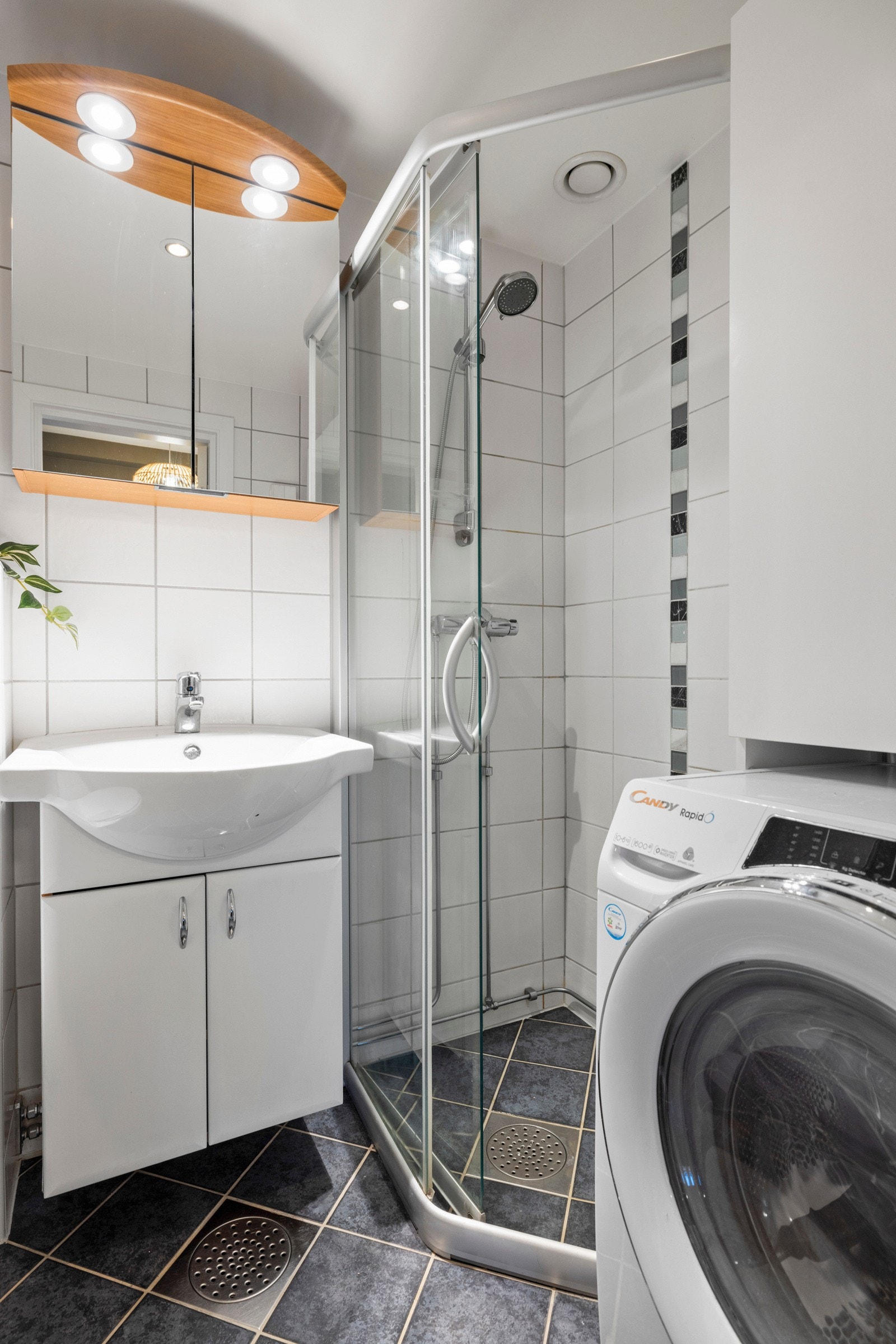 Badet har et vegghengt toalett, et dusjhjørne og opplegg for vaskemaskin Galleribilde