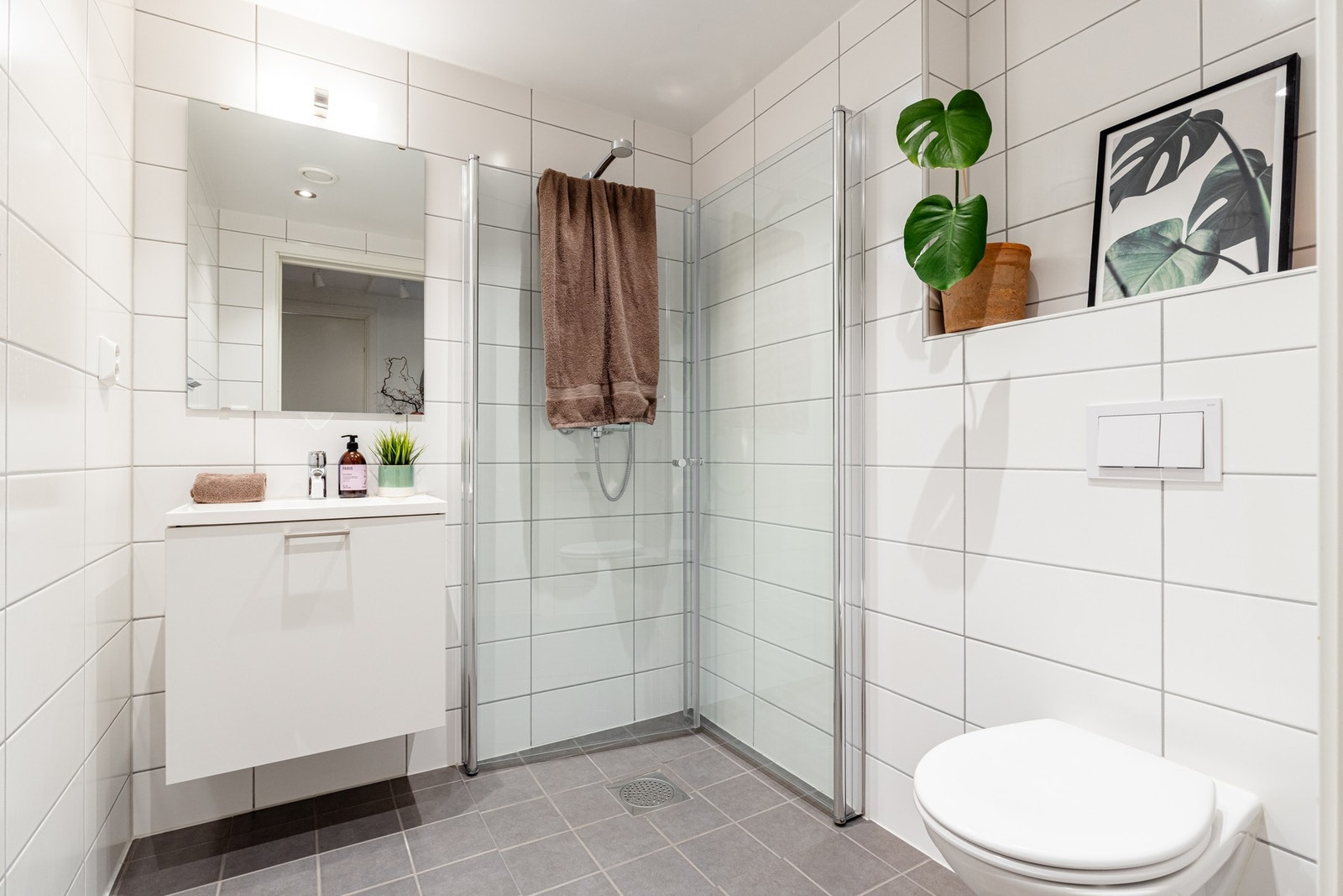 Begge badene er tidløst innredet med lyse fliser, downlights i taket, gulvvarme og pene oppbevaringsmøbler. Galleribilde