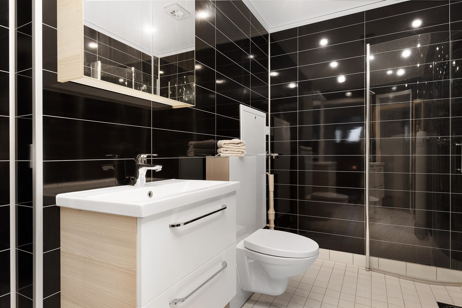 Stilrent baderom med våtromsplater på vegger og flislagt gulv. Dusjnisje, vegghengt toalett, baderomsinnredning med heldekkende servant. Galleribilde