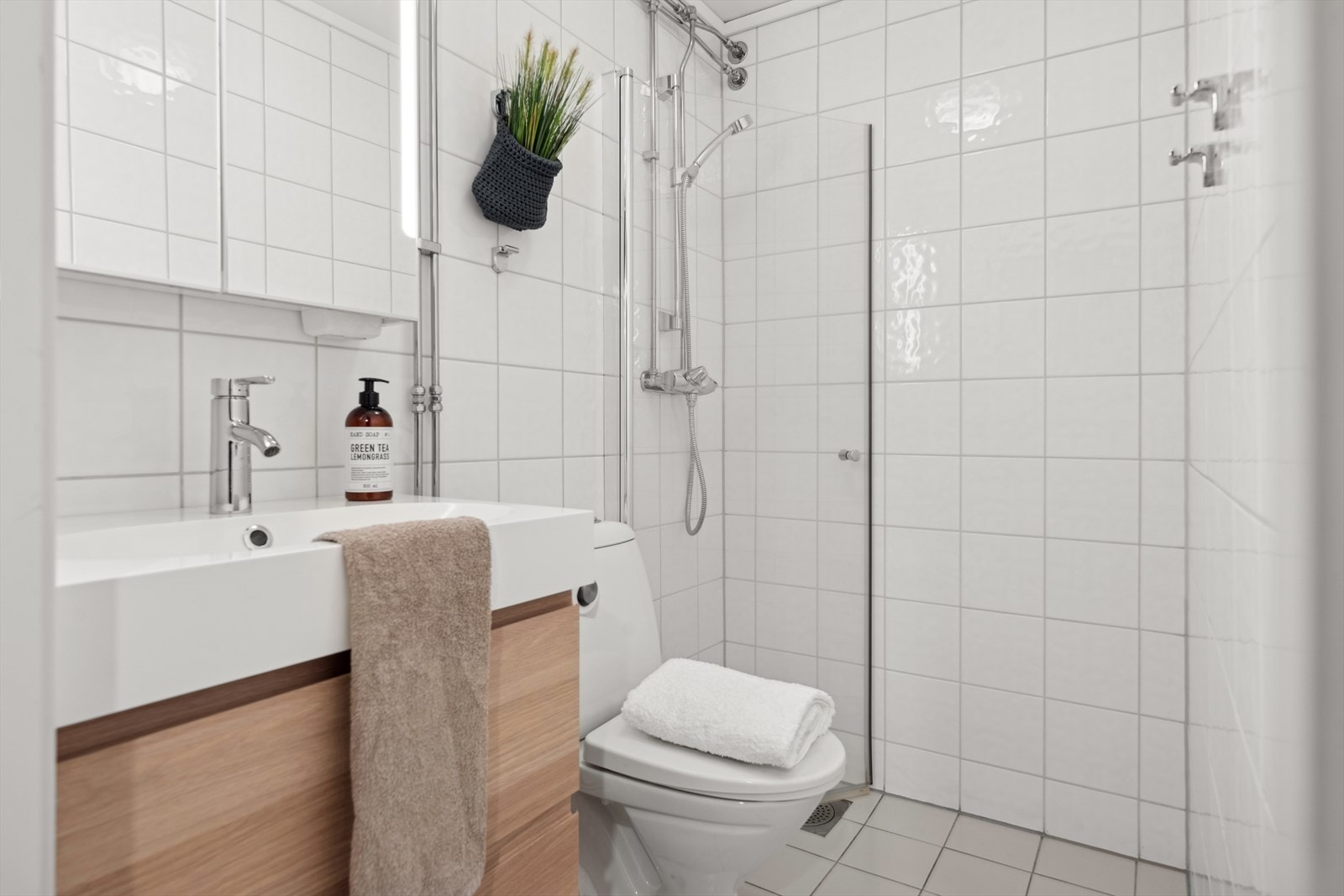 Badet er innredet med et toalett, dusj med innfellbar dusjdør, moderne baderomsinnredning med heldekkende servant og speilskap med lys. Galleribilde