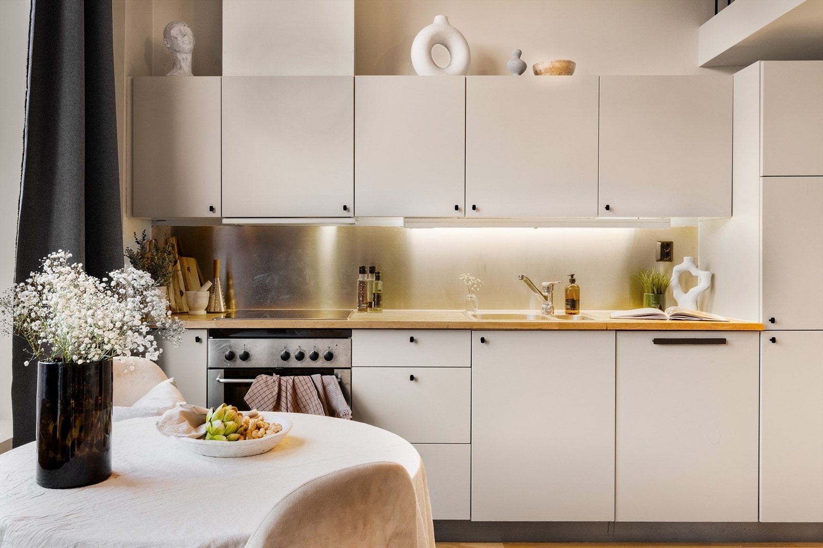 Kjøkkenet er i en åpen løsning og innredet med moderne, beige matte fronter og en heltre benkeplate med nedfelt oppvaskkum. Galleribilde