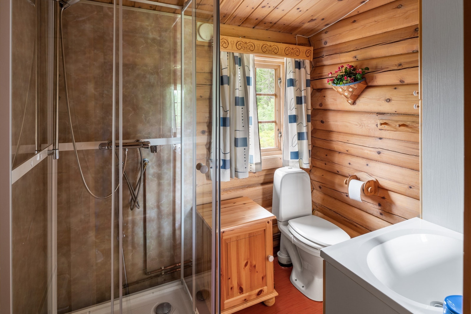 Baderommet har ubehandlet tømmer på veggene og rødt belegg på gulvet. Galleribilde