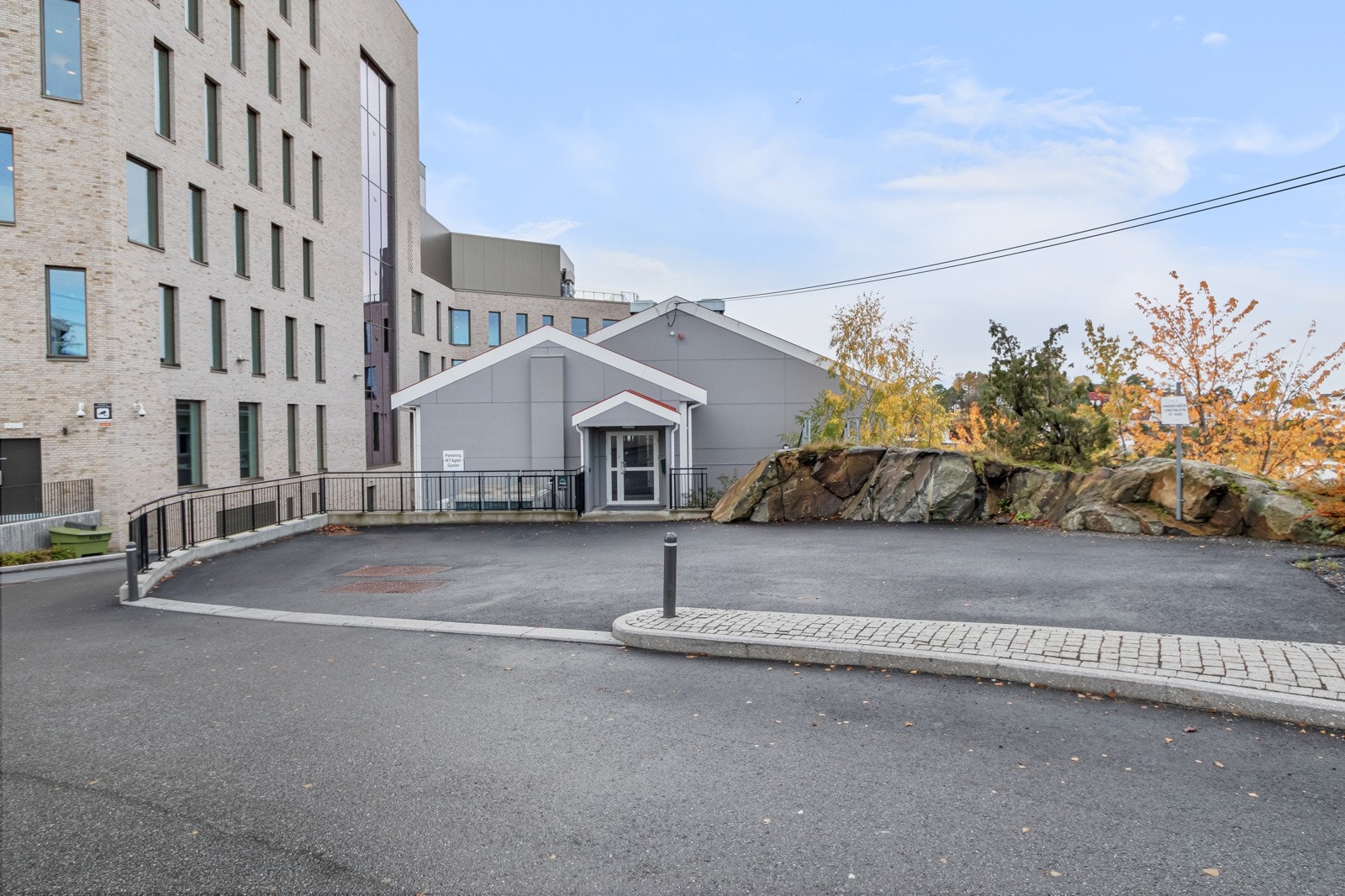 Det er en asfaltert parkeringsplass på tomten som er tilhørende bygget. Dette er ved en av hovedinngangene. Galleribilde