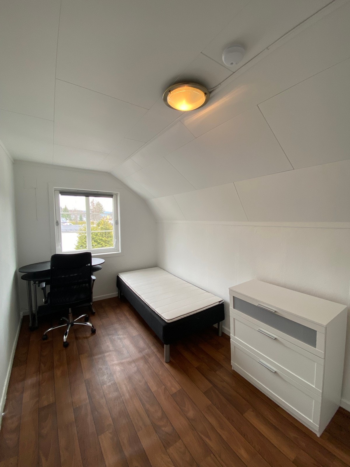 Seng, kommode, taklampe, vindu, gardin, skrivebord og stol Galleribilde