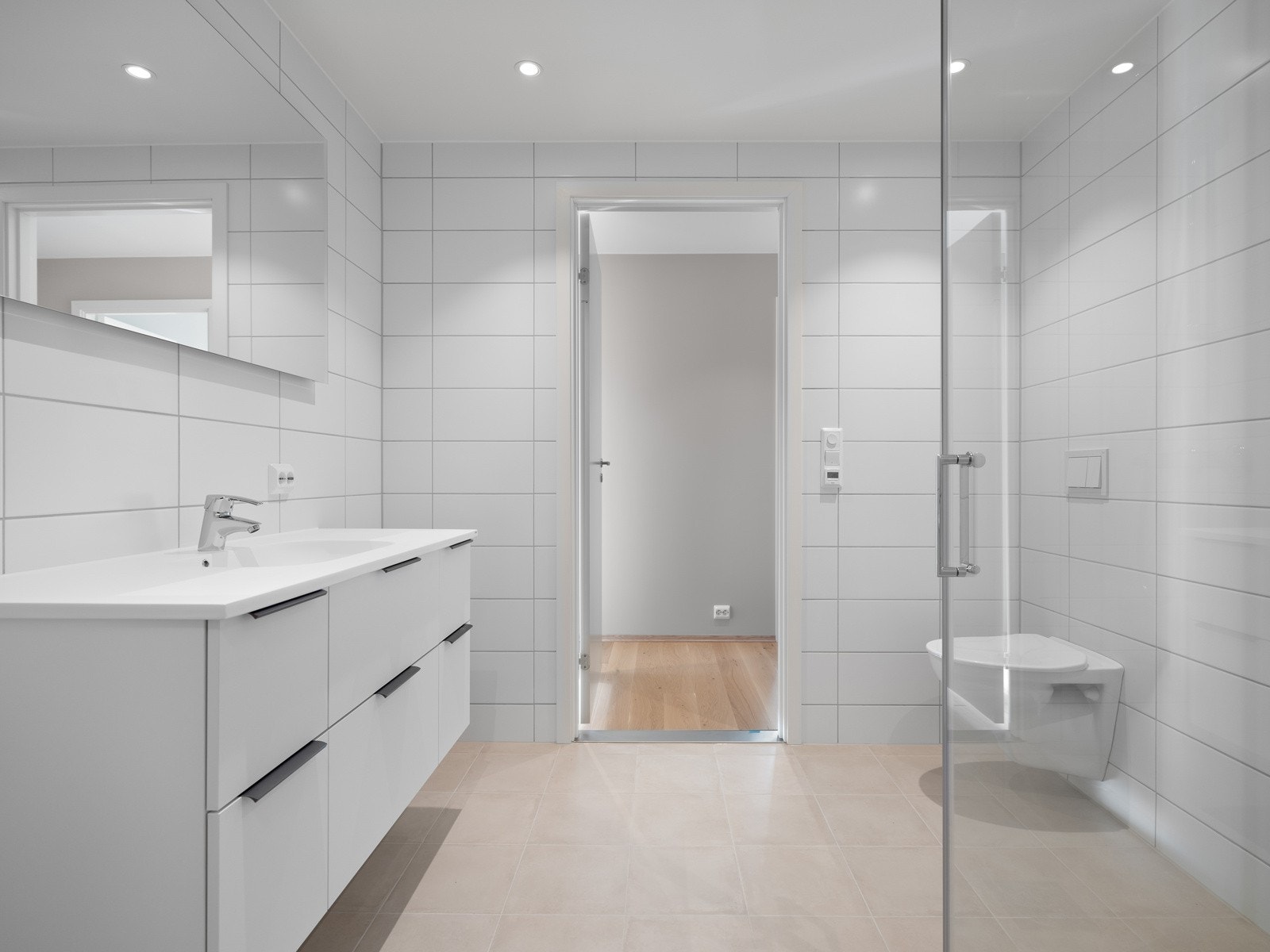 Videre er badet utstyrt med veggmontert toalett og dusjhjørne med innfellbare dusjdører i glass. Fra badet er det en skyvedør videre inn til bod/vaskerom. Galleribilde