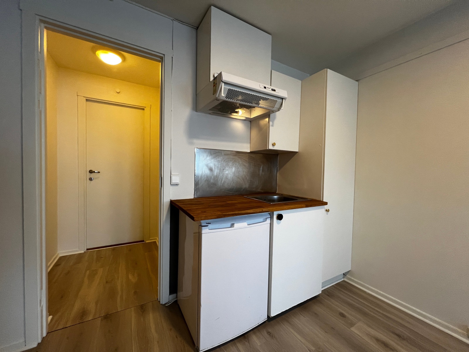 Avtrekksvifte, servant og kjøleskap under benkeplate. Stort høyskap på høyre side. Leiligheten har vært utleid, og leietager har benyttet en frittstående komfyr med koketopp som har stått på benkeplaten Galleribilde