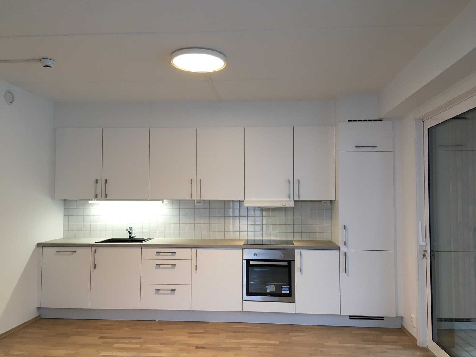 Kjøkken med hvitevarer og utgang til romslig balkong Galleribilde