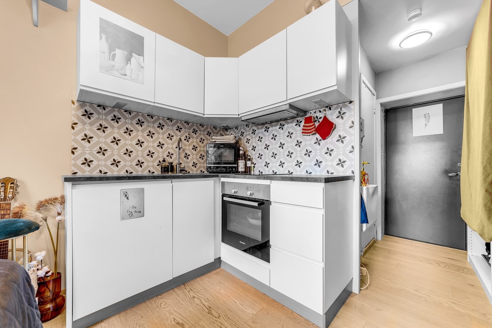 Kjøkkeninnredning med glatte fronter. Belysning under overskap. Fliser på vegg over benkeskap. Laminat benkeplate med nedfelt kum i rustfritt stål. Ventilator. Induksjonstopp, stekeovn og kjøl er integrert i innredningen. Galleribilde