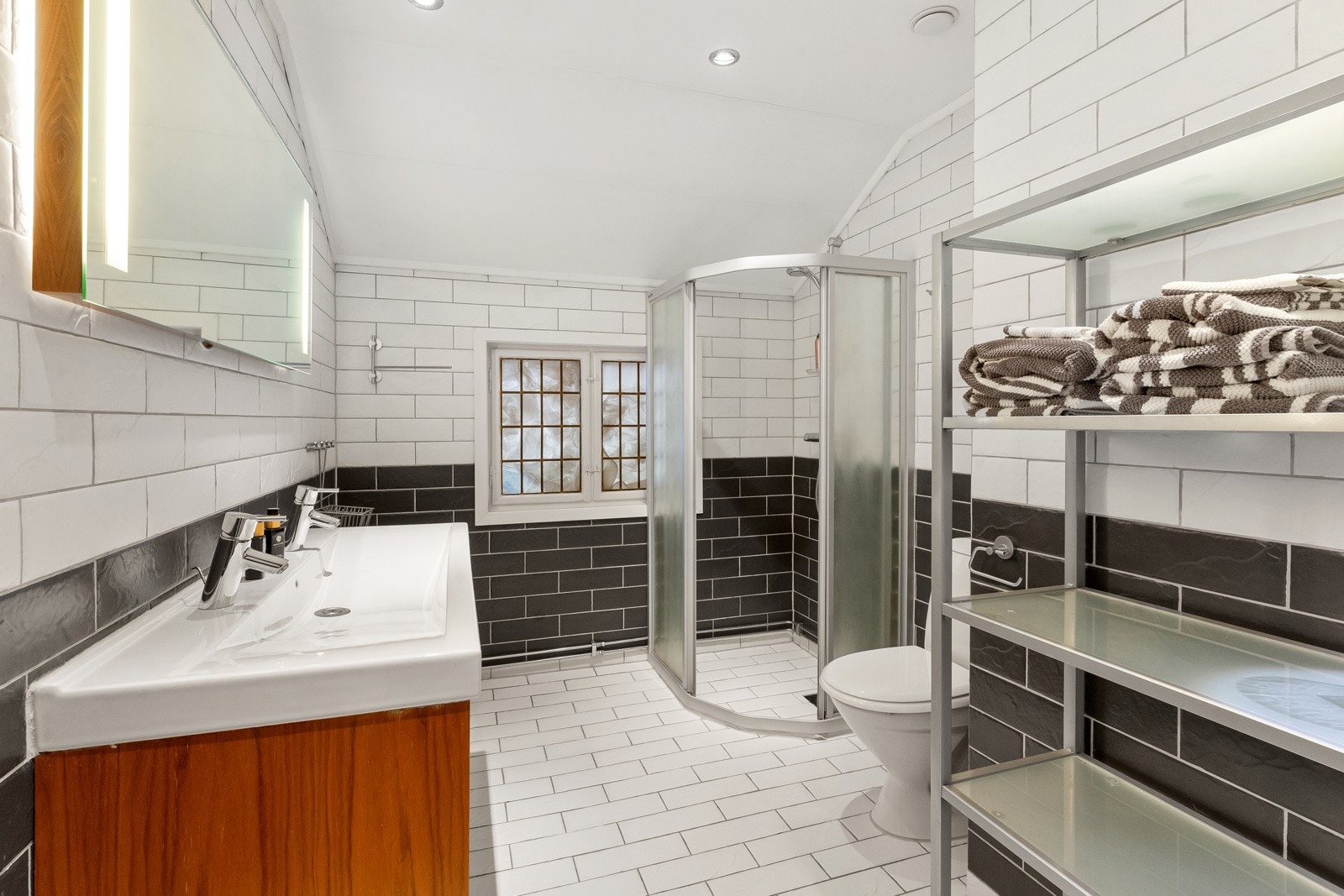 Det andre badet har et delikat uttrykk der hvite gulvfliser med varme kombineres med sorte og hvite fliser på veggene. Galleribilde