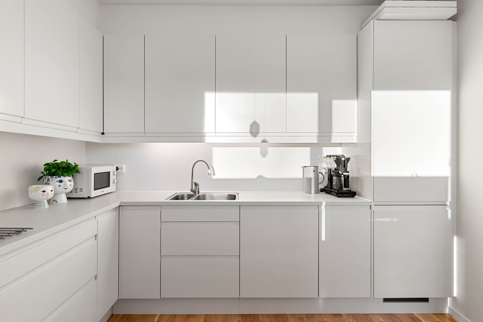 Lekkert tidløst kjøkken med hvit innredning og nedfelt vask. Spottbelysning over benk. Galleribilde