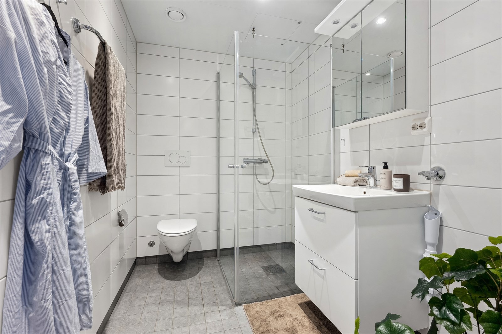 Lyst og flislagt baderom med varmekabler i gulv og downlights i himling. Innredningen består av servantslap, speilskap og dusjsone. Det er opplegg for vaskemaskin på badet og mekanisk avtrekk. Galleribilde