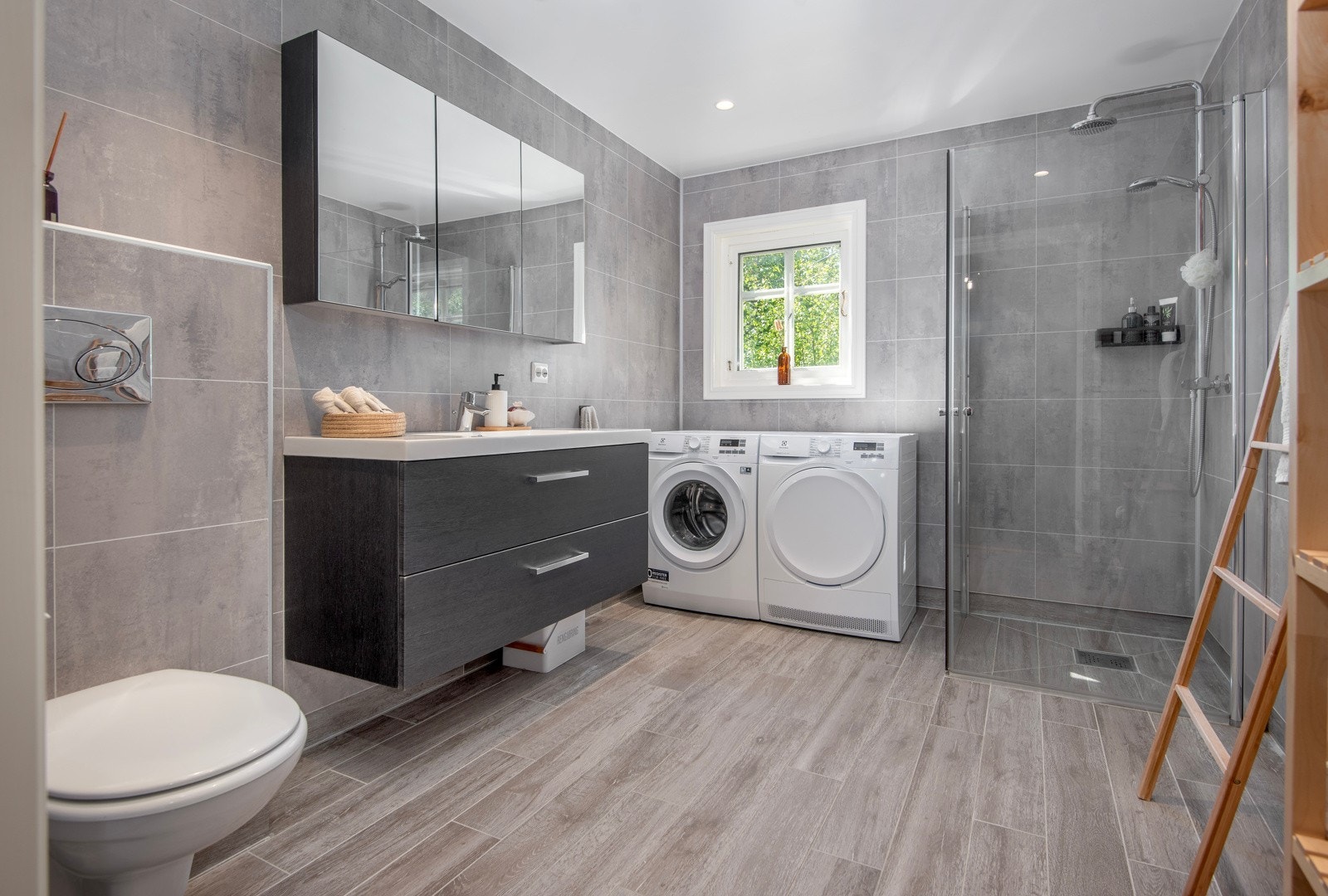 Innbydende og romslig bad/vaskerom fra 2018 belagt med våtromsplater på vegger og fliser på gulv med elektriske varmekabler. Innredet med dusjhjørne, vegghengt toalett - Galleribilde